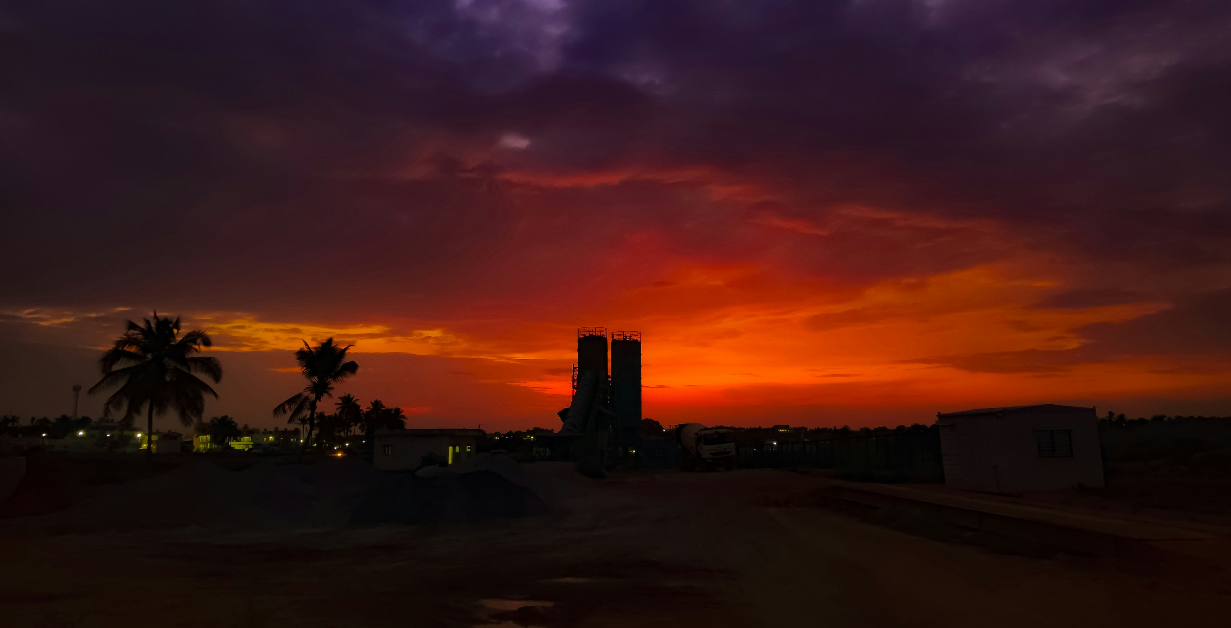 Dramatic sunset over industrial silhouette with palm trees