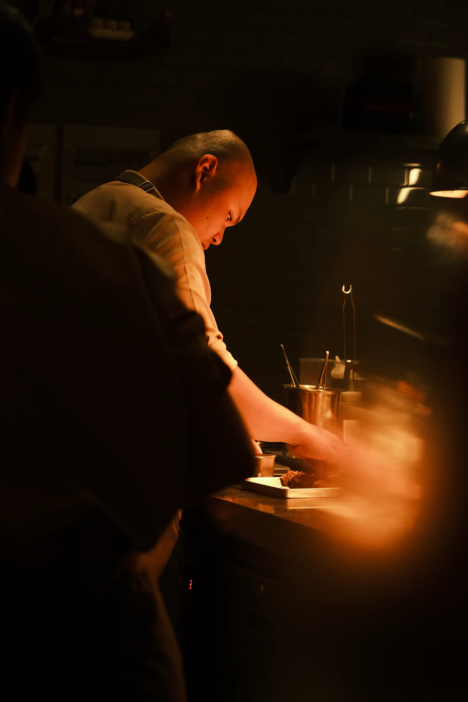 A chef working at the pass in a dimly lit kitchen