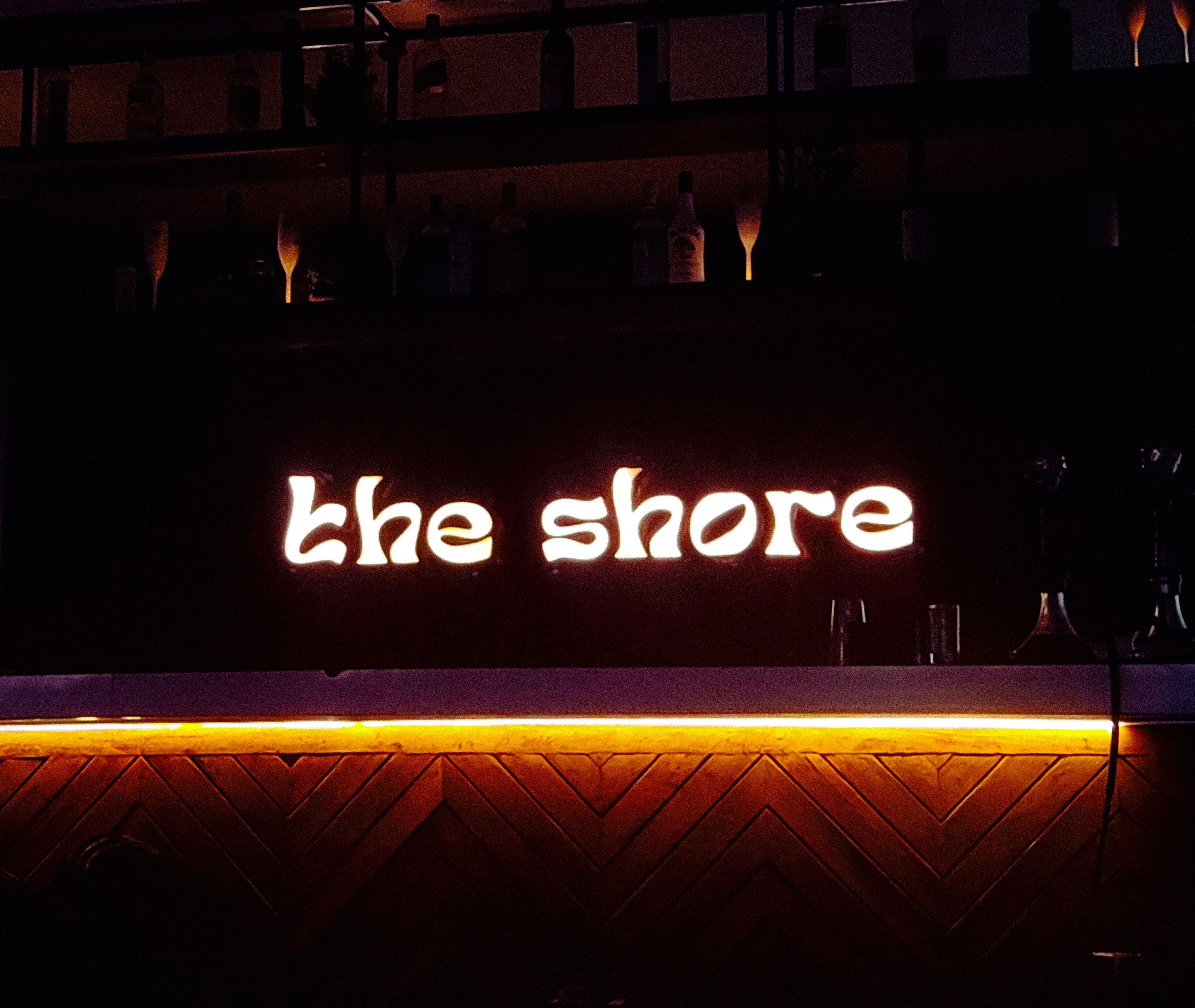 Illuminated sign for "the shore" above bar