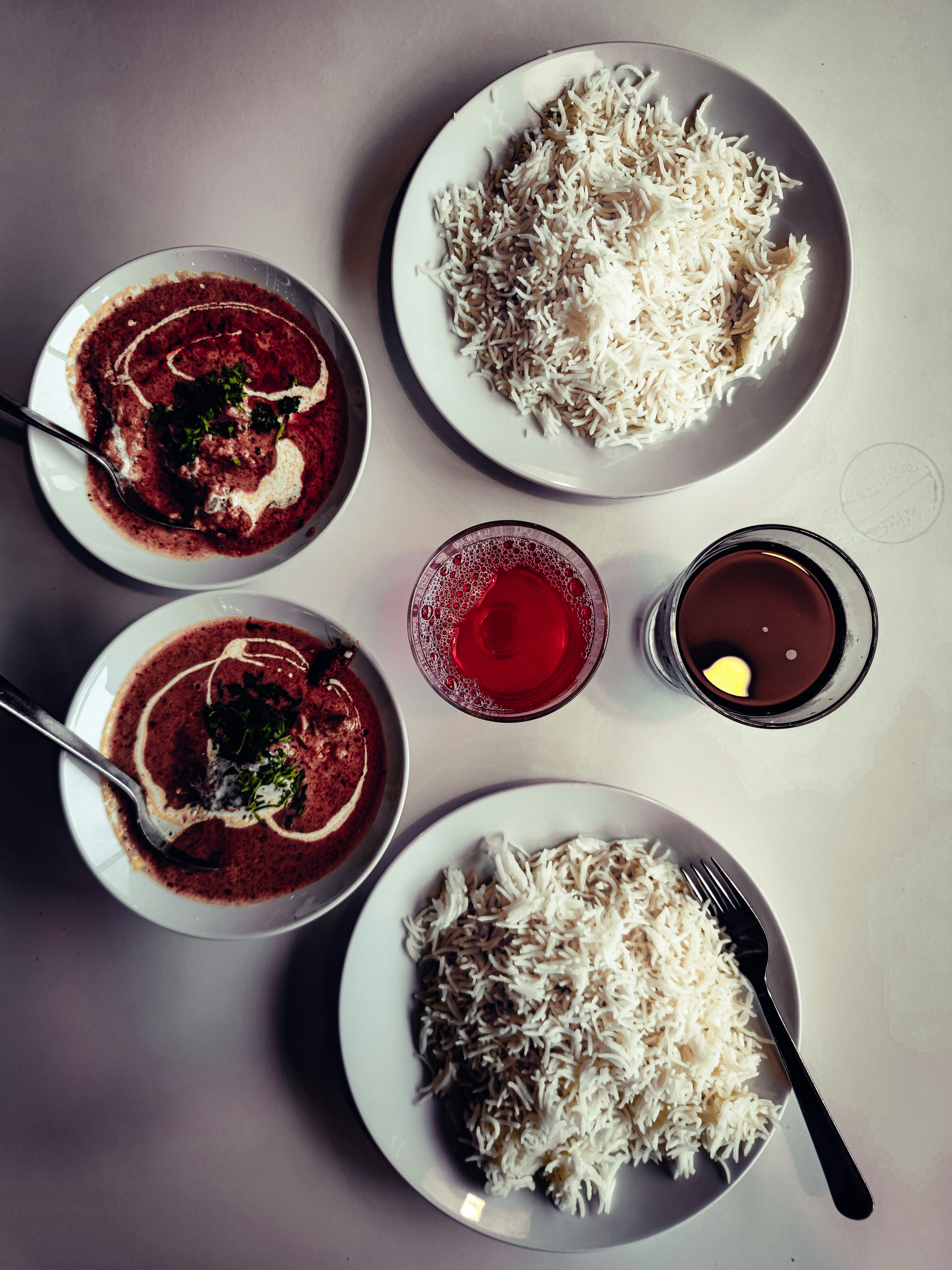Two bowls of a dark, creamy curry finished with a swirl of cream and chopped coriander, with plates of basmati rice