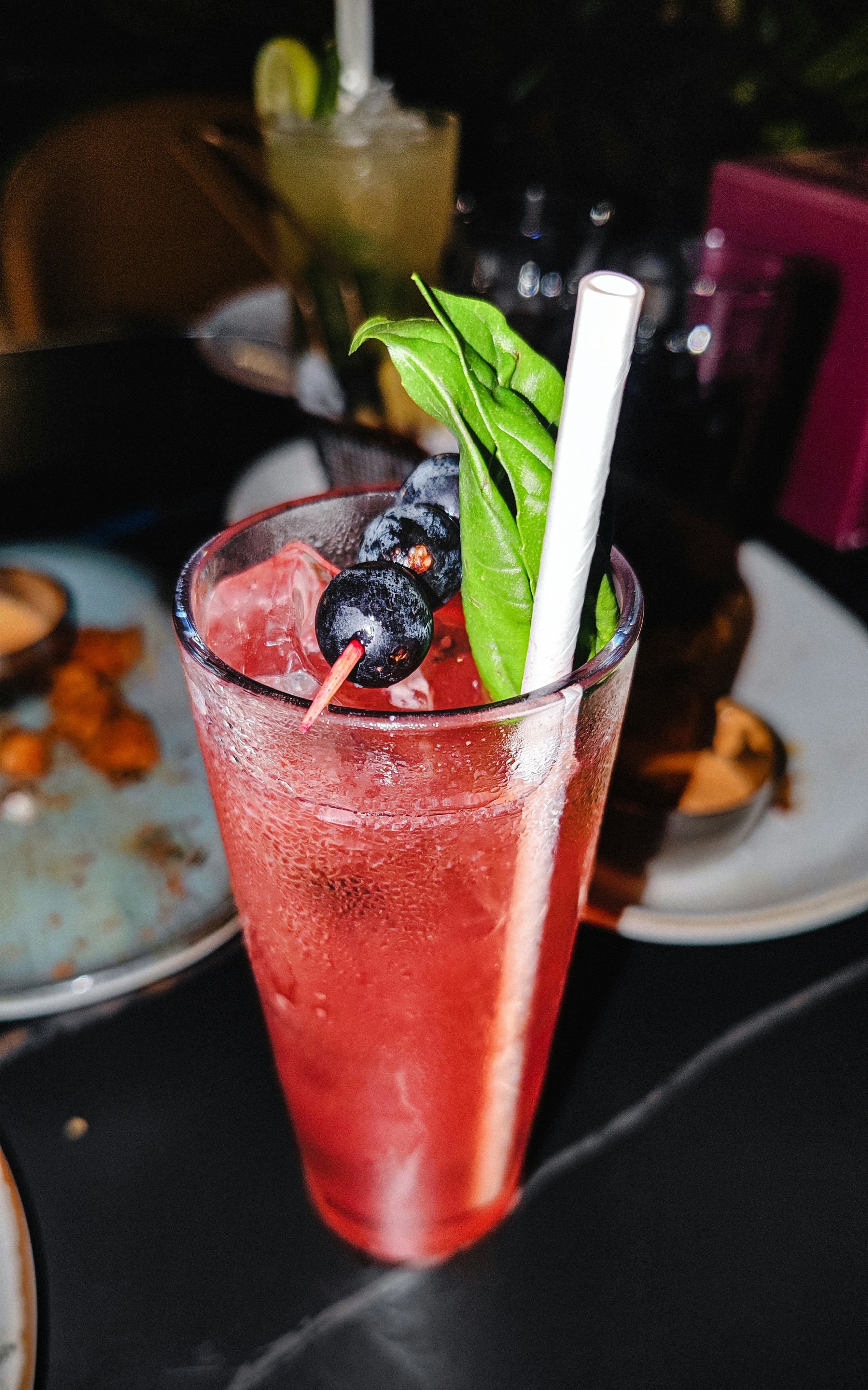 Red cocktail with blueberries and basil garnish