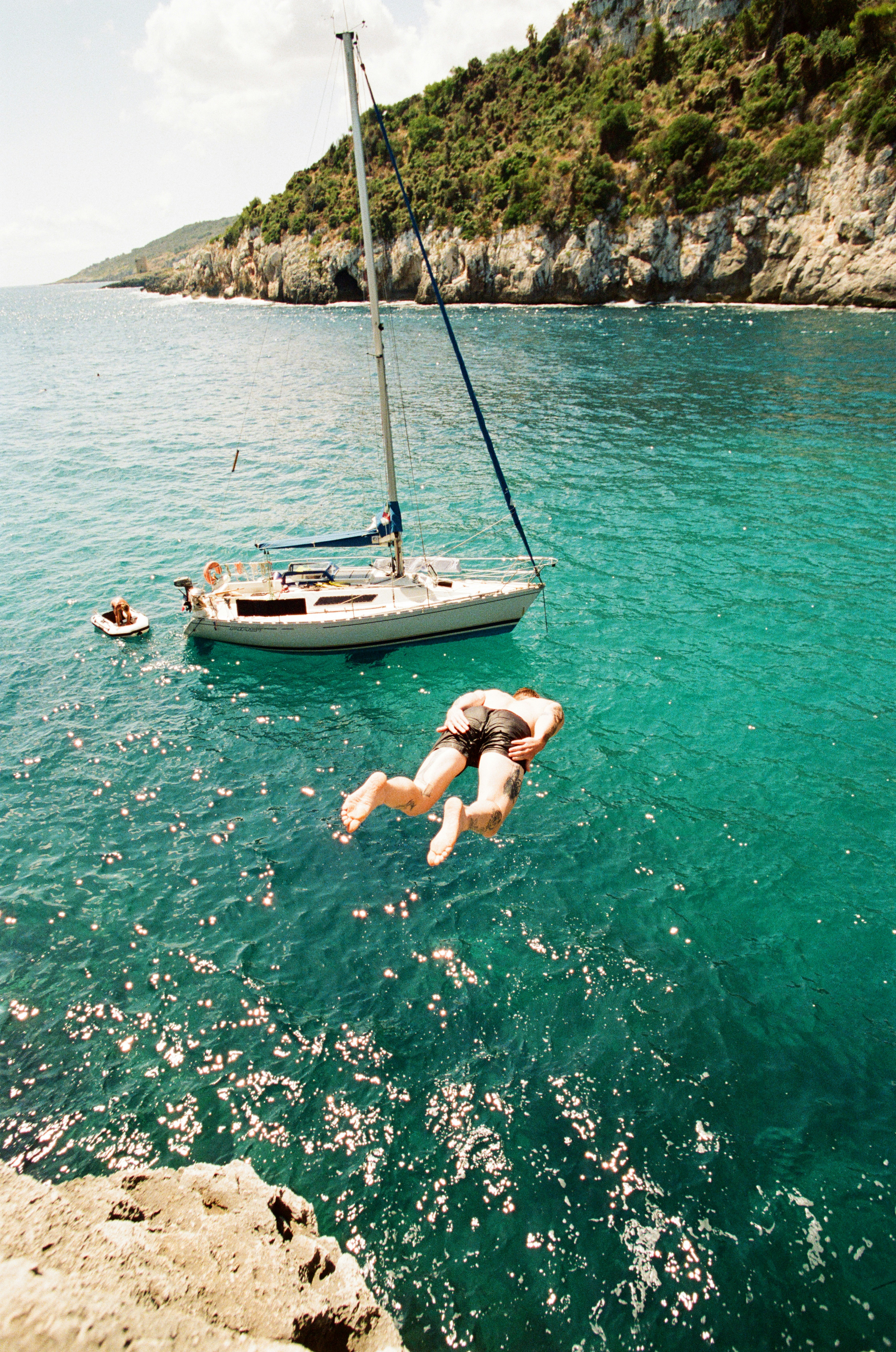 Man jumps from cliff into turquoise ocean water