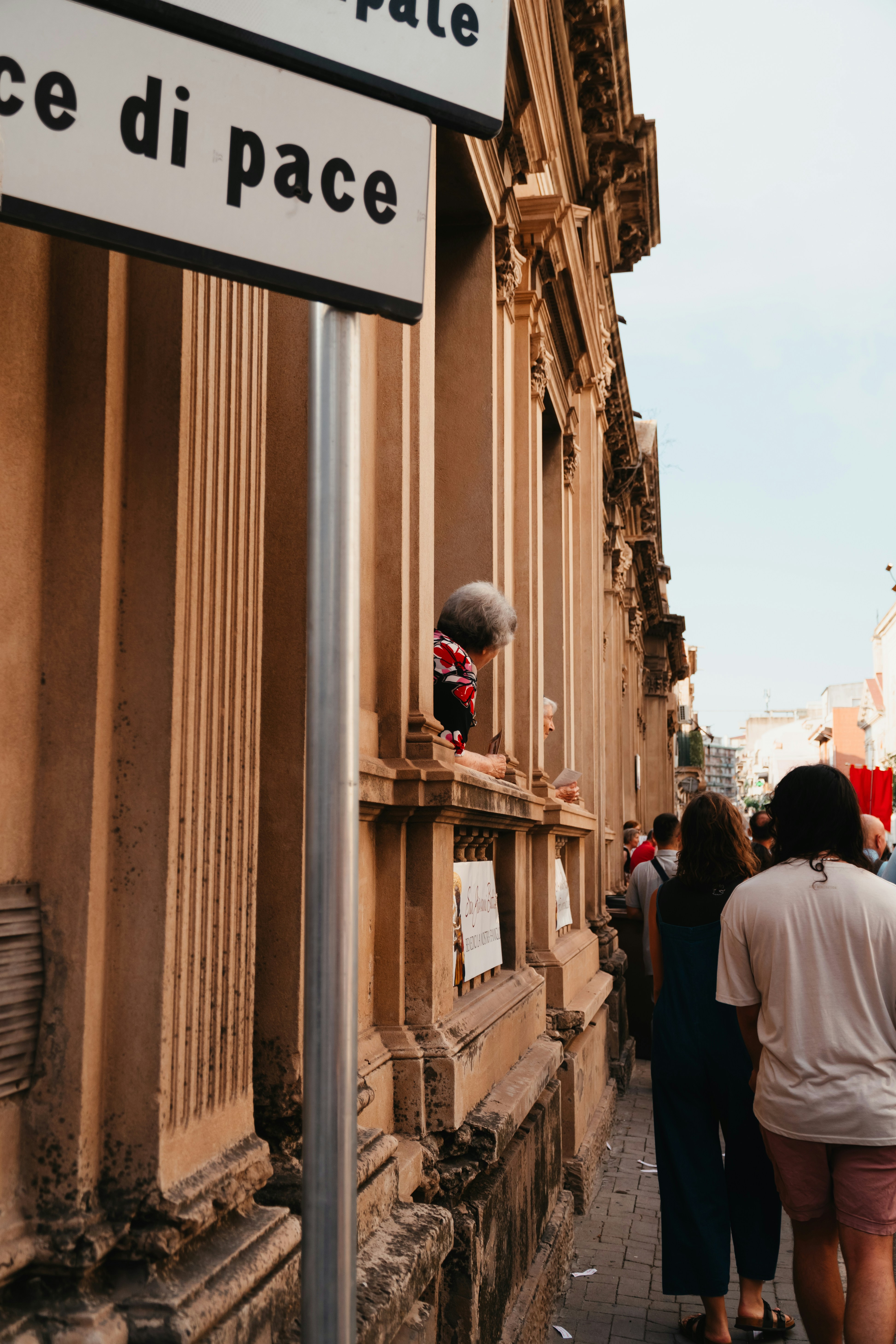 People walk past a building with a sign reading "di pace".