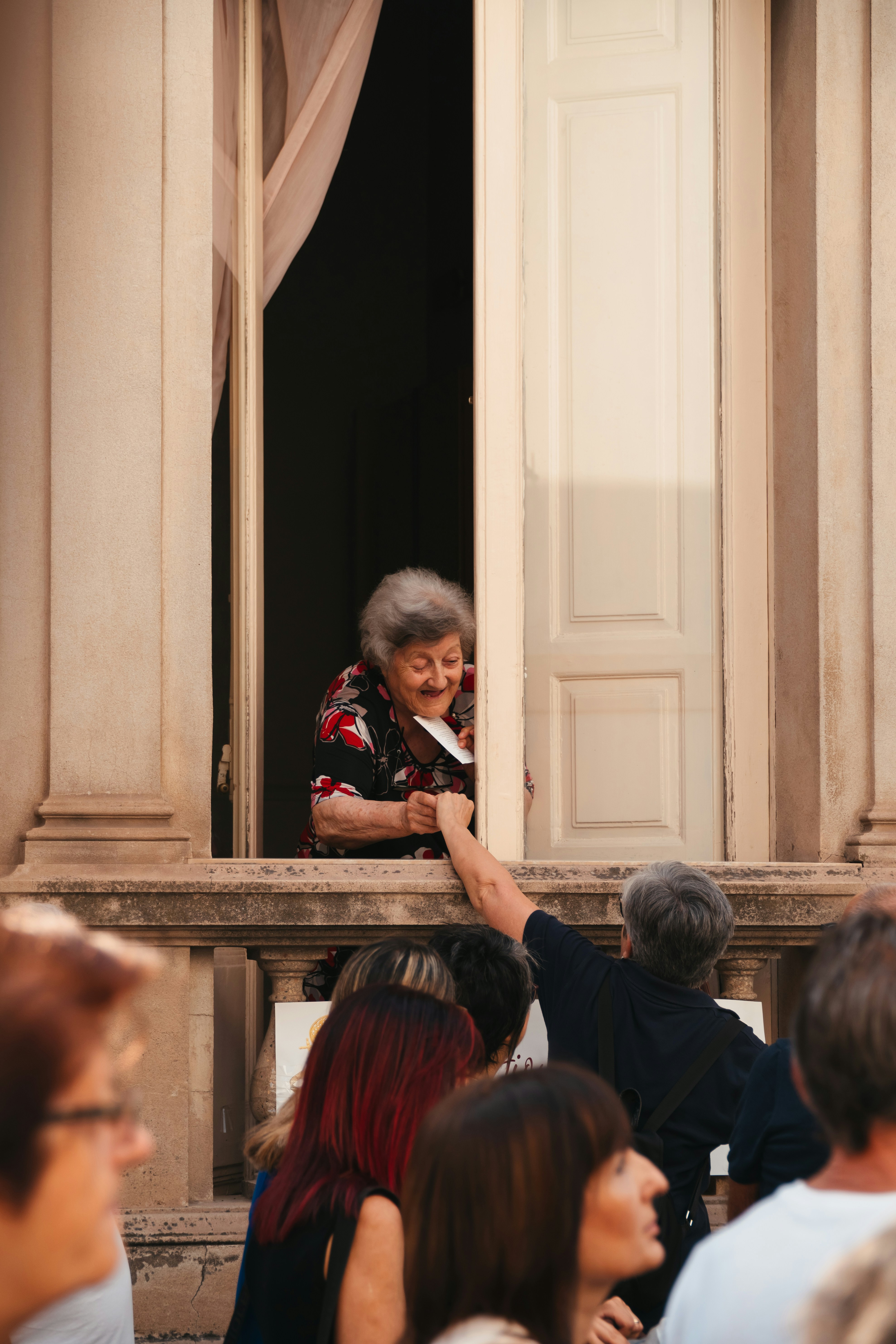 Woman hands object from window to person below