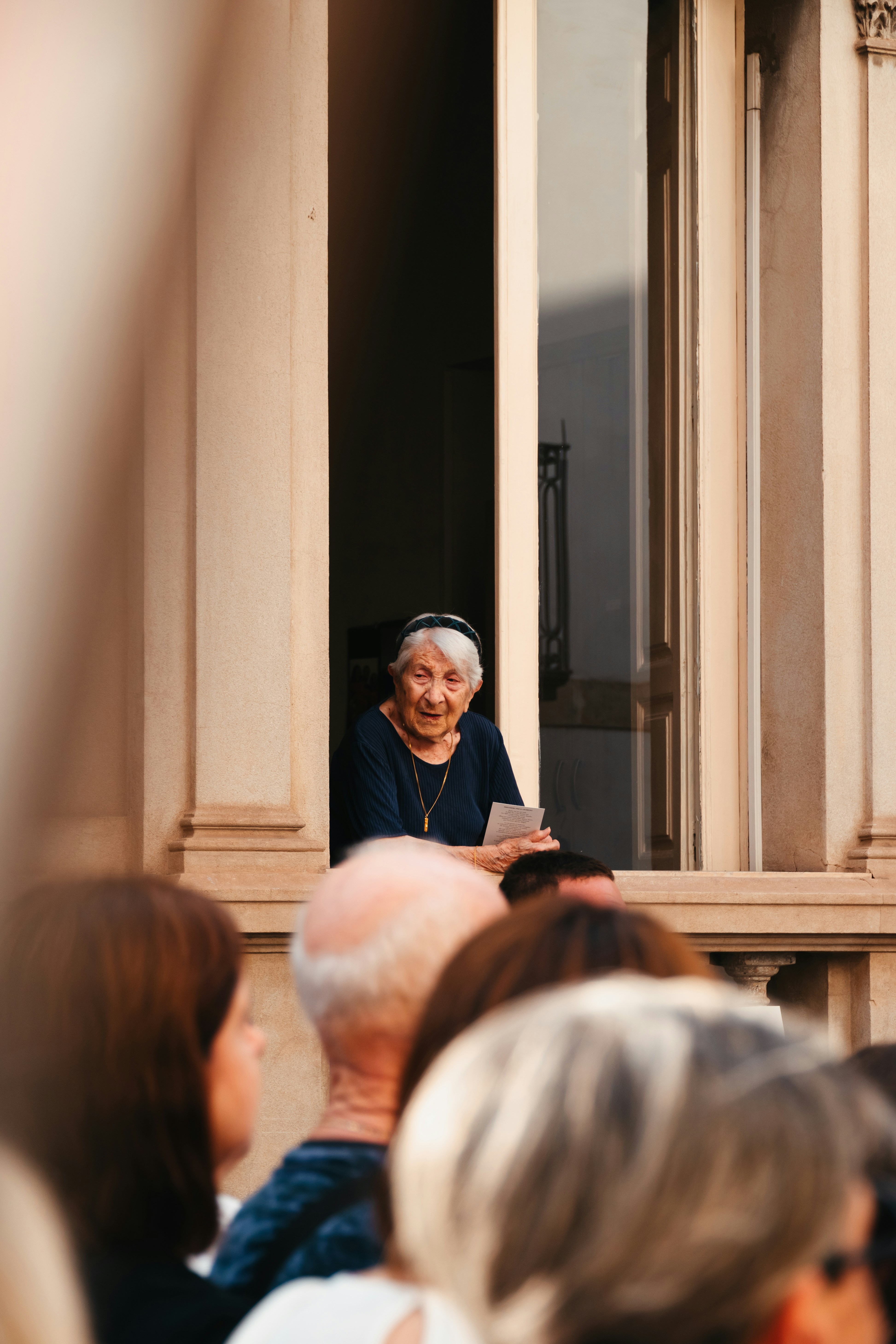 Elderly woman looking out a window at a crowd