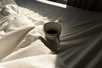 Mug of coffee on rumpled white bedding