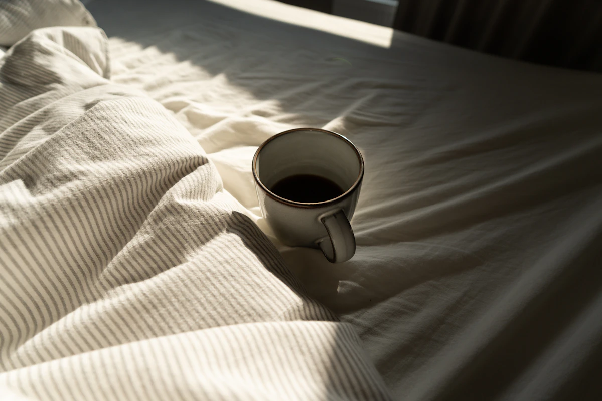 Une tasse posée sur un lit aux draps blancs froissés