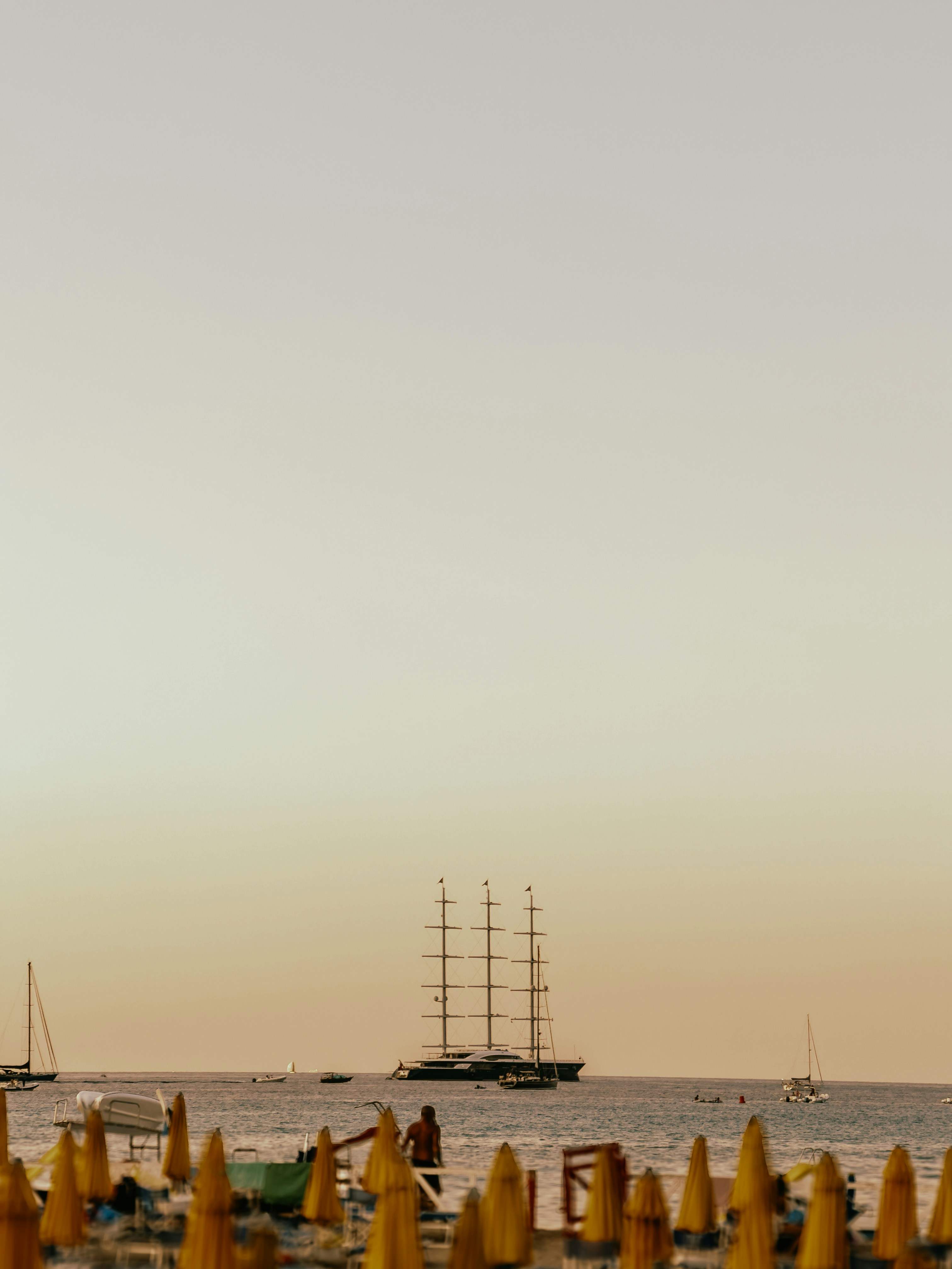 Sailboat on the ocean near a beach with umbrellas