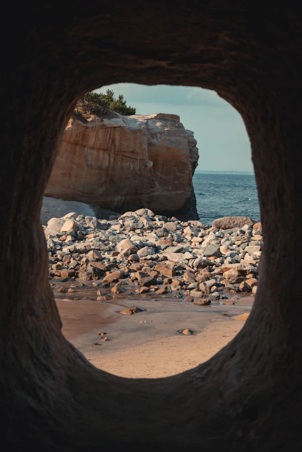 View through a cave opening to a rocky beach and ocean.