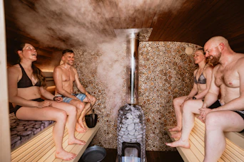 People relaxing in sauna with steam and wooden benches