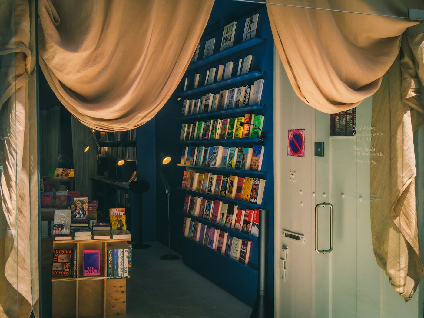 A bookstore entrance with draped linen curtains, a display table, and books on deep blue wall shelves
