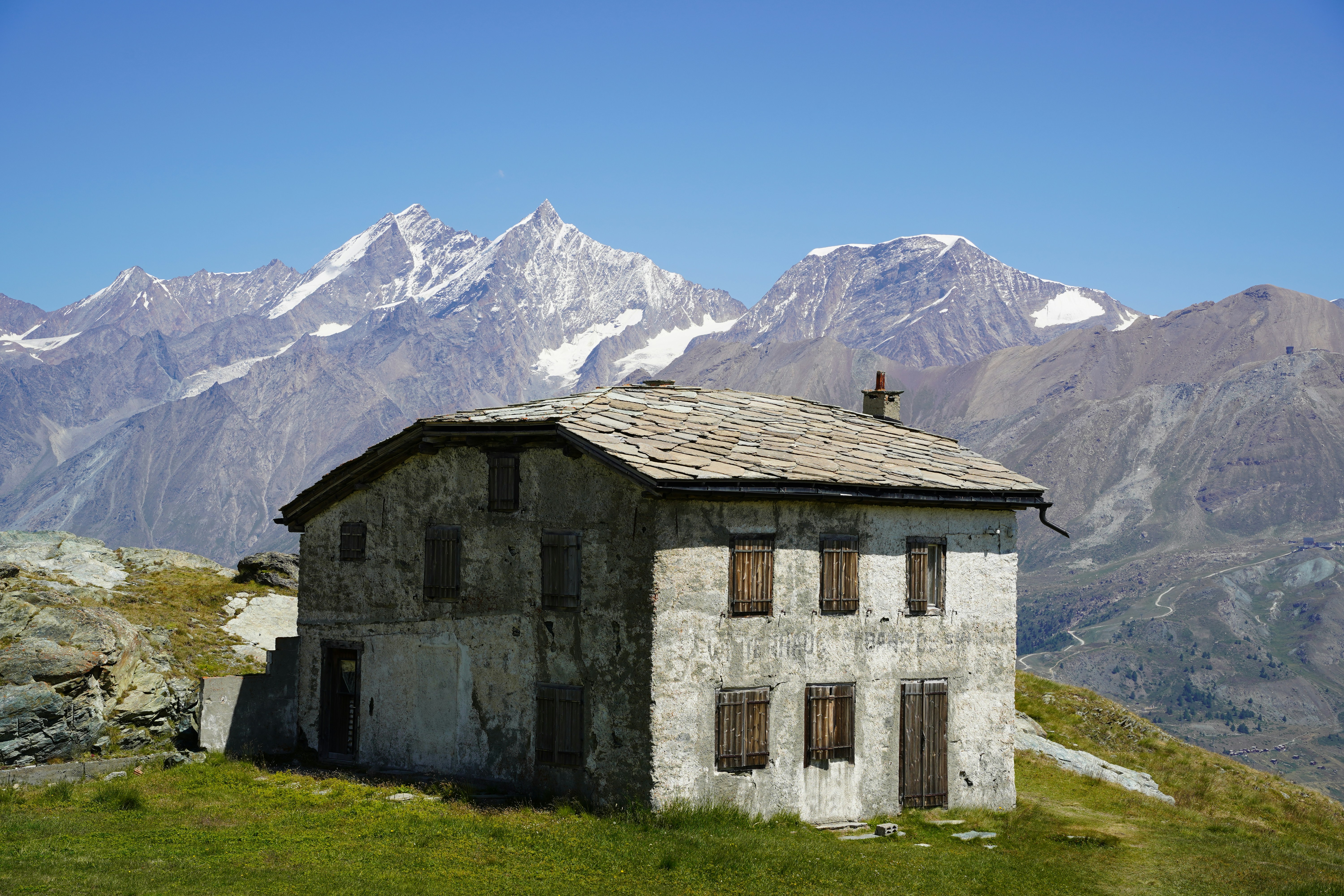 Old stone house on a grassy hill with mountains.