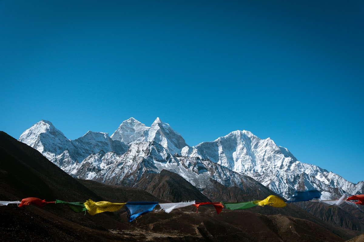 Snow-capped Himalayan peaks under a clear blue sky with strings of colorful prayer flags in the foreground