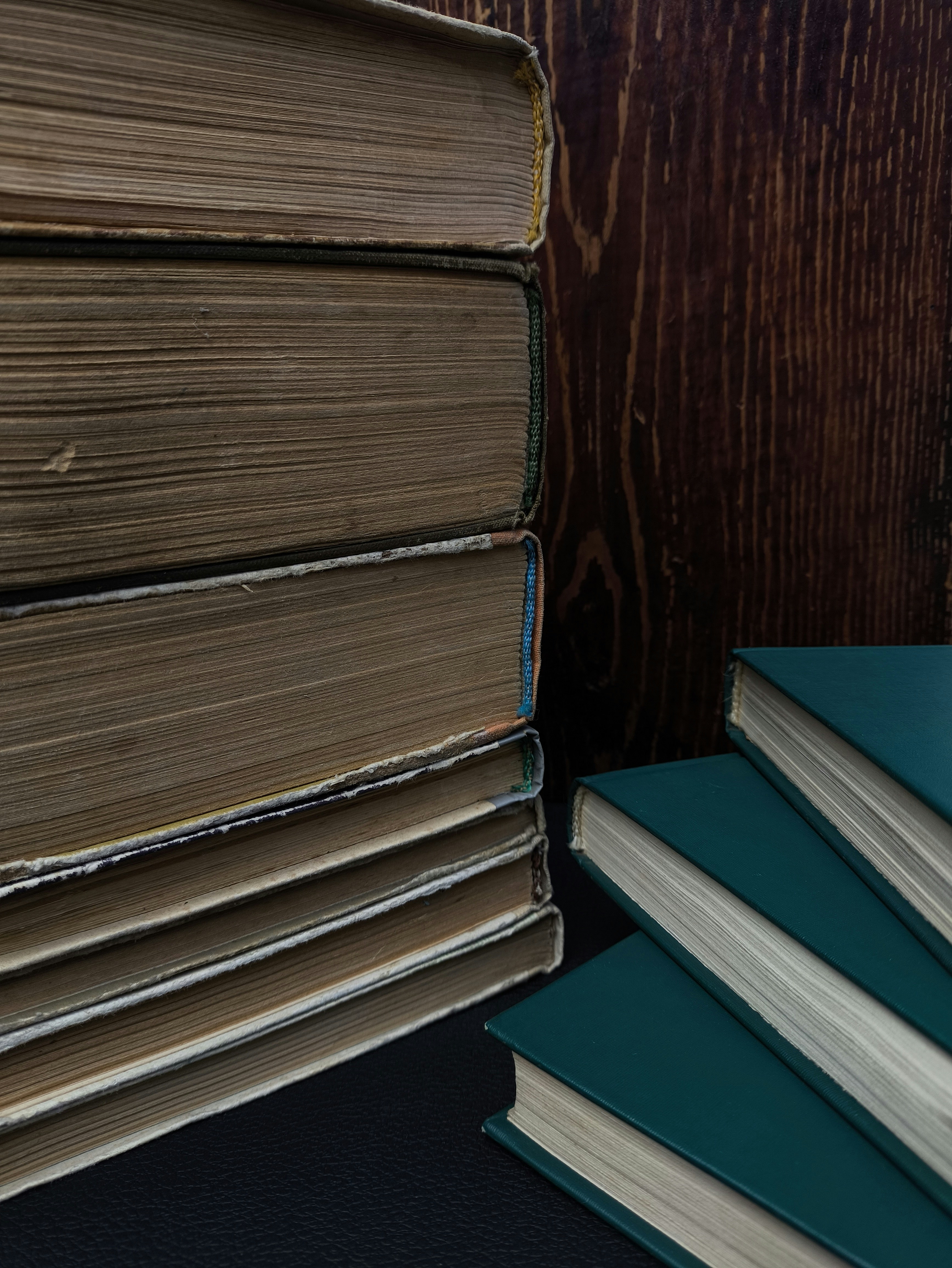 Stack of old books beside teal books on wood.