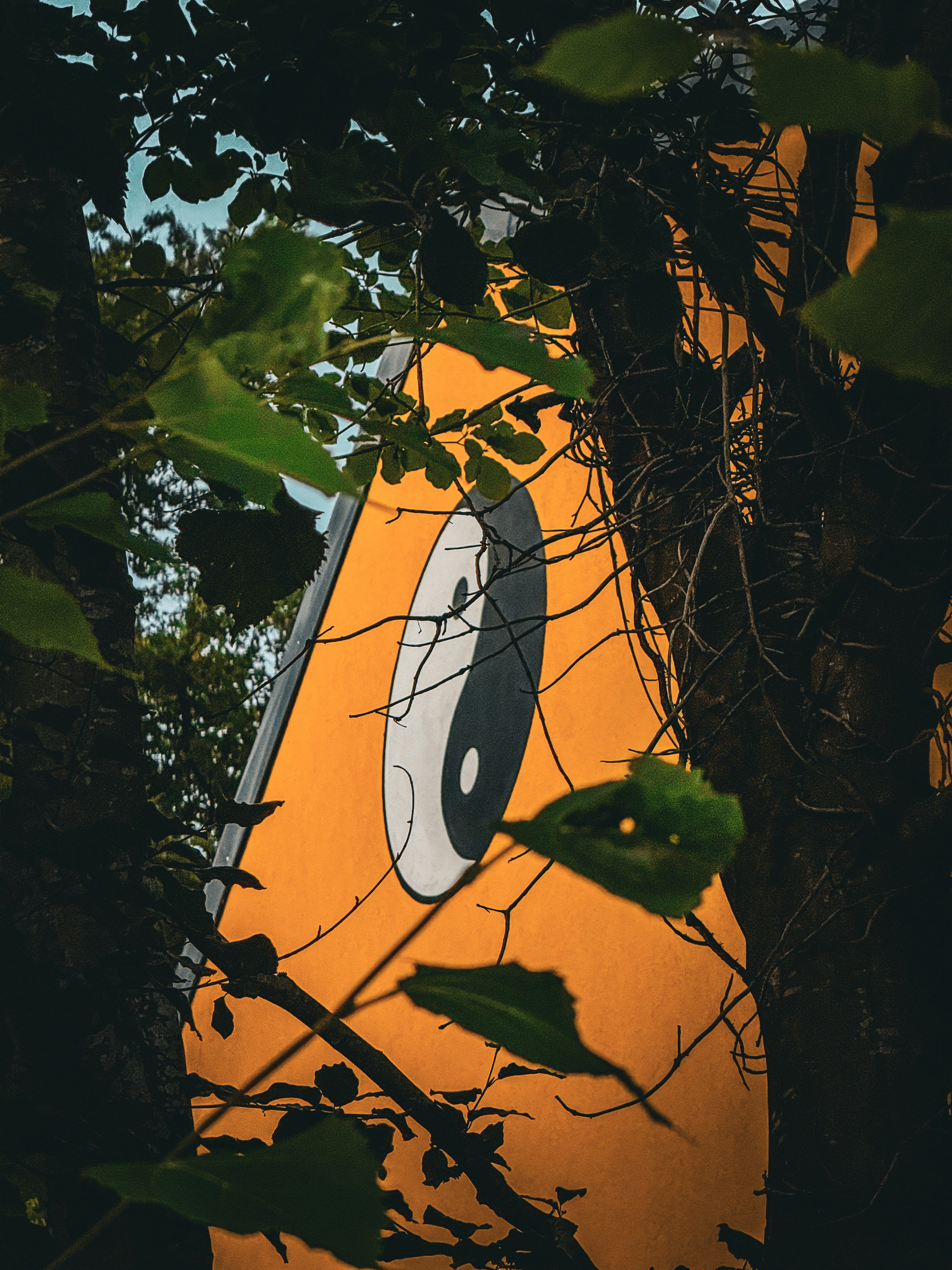 Struttura arancione con un simbolo yin yang parzialmente nascosto da foglie