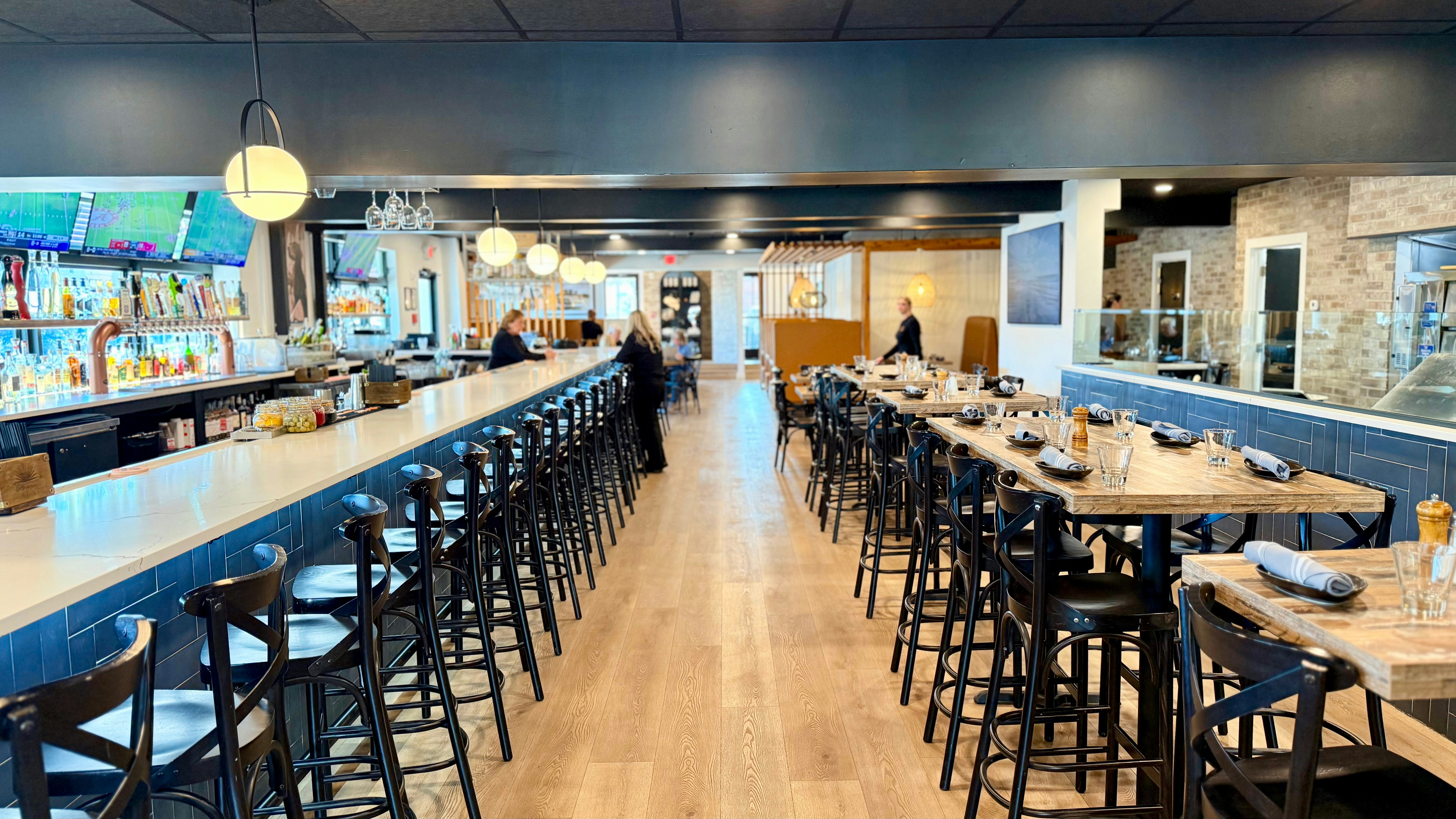 Modern restaurant interior with long bar and dining tables.