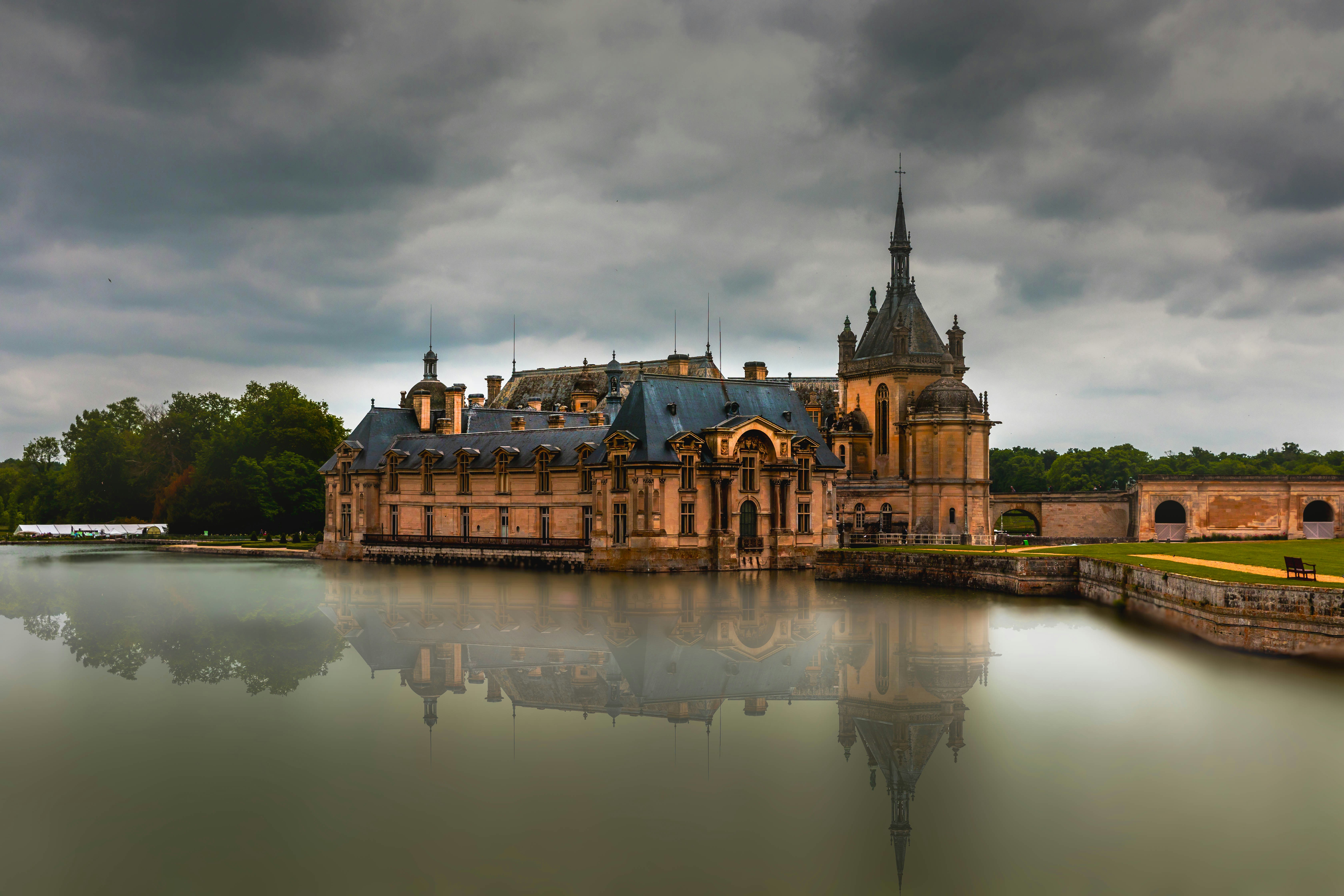 Grand chateau reflected in calm water under cloudy sky