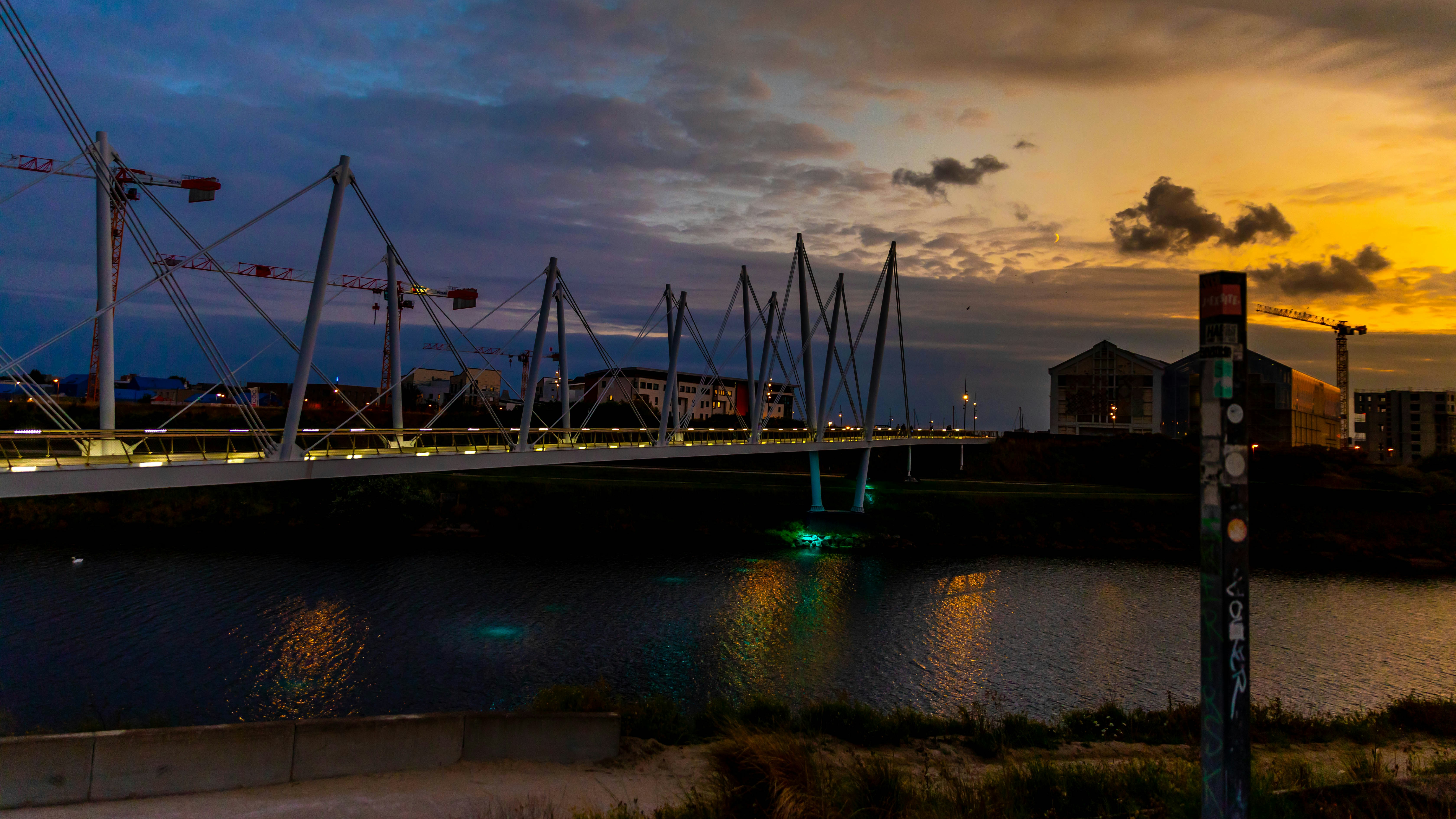 Modern bridge over water at dusk with city lights.