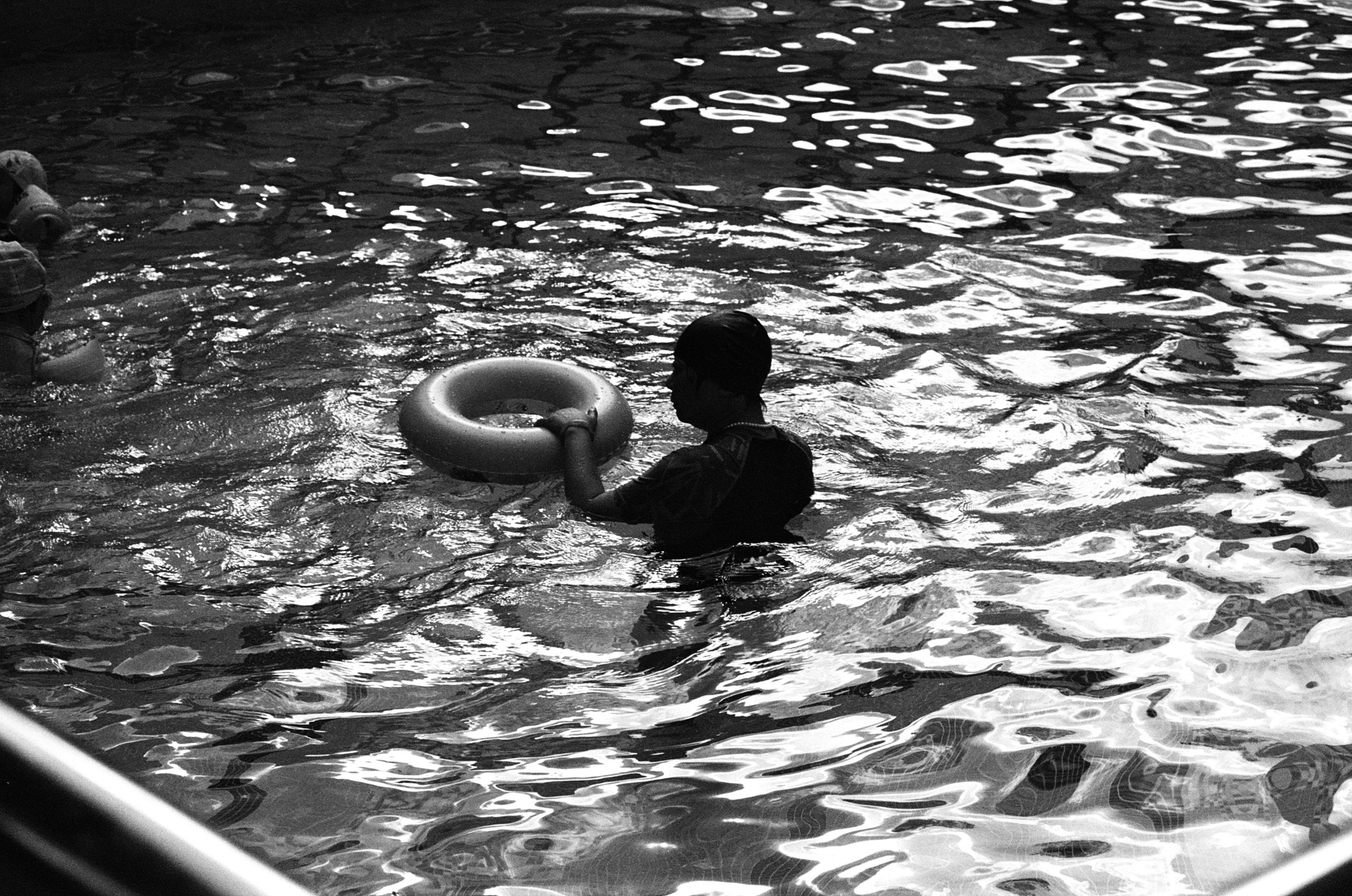 Su kenarında endişeli ve tereddütlü bir şekilde bekleyen, su korkusu ve geçmiş travmaların psikolojik etkilerini simgeleyen bir kişi.