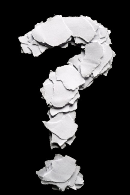 Torn paper pieces form a question mark on black background