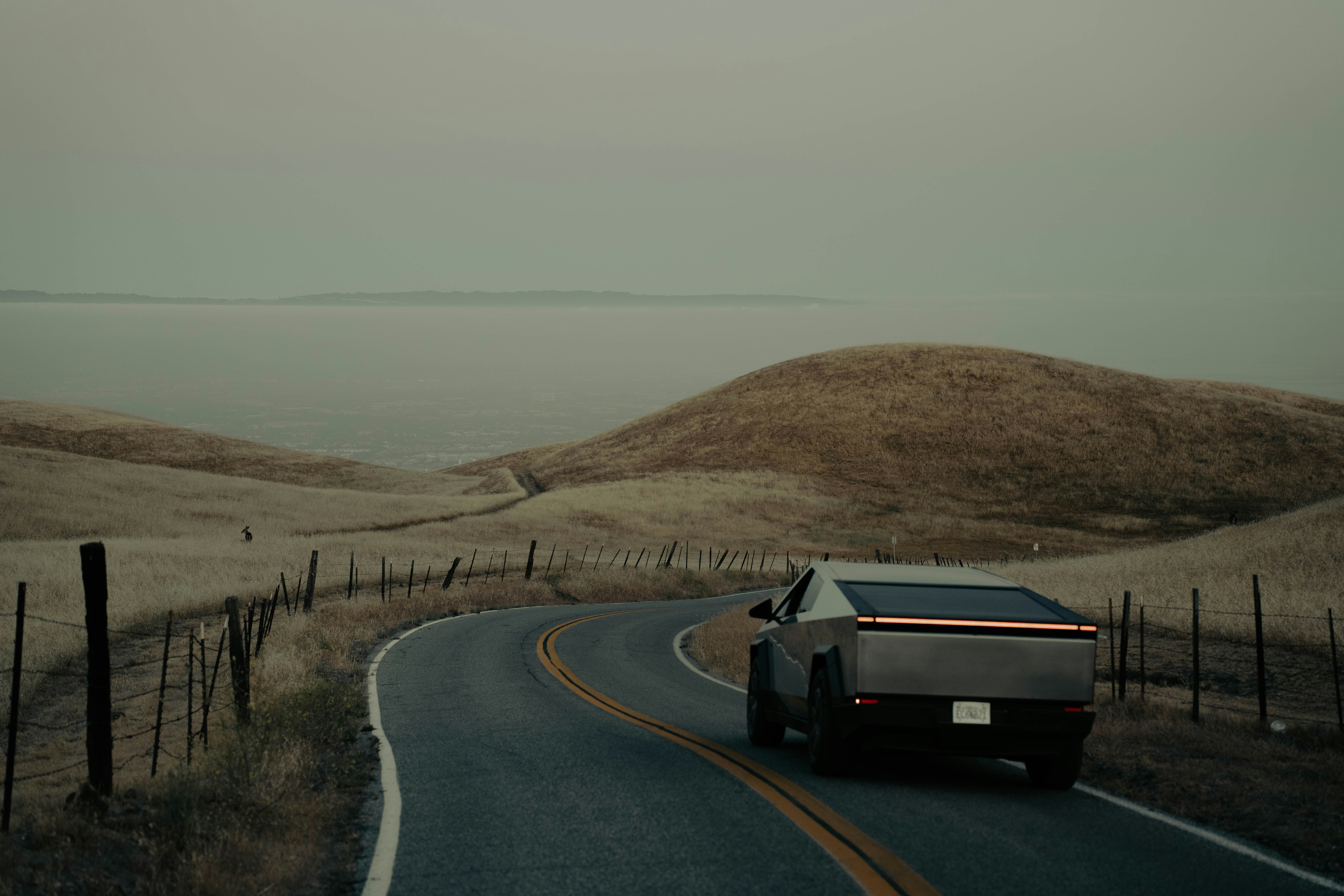 Electric truck drives on winding road near ocean.