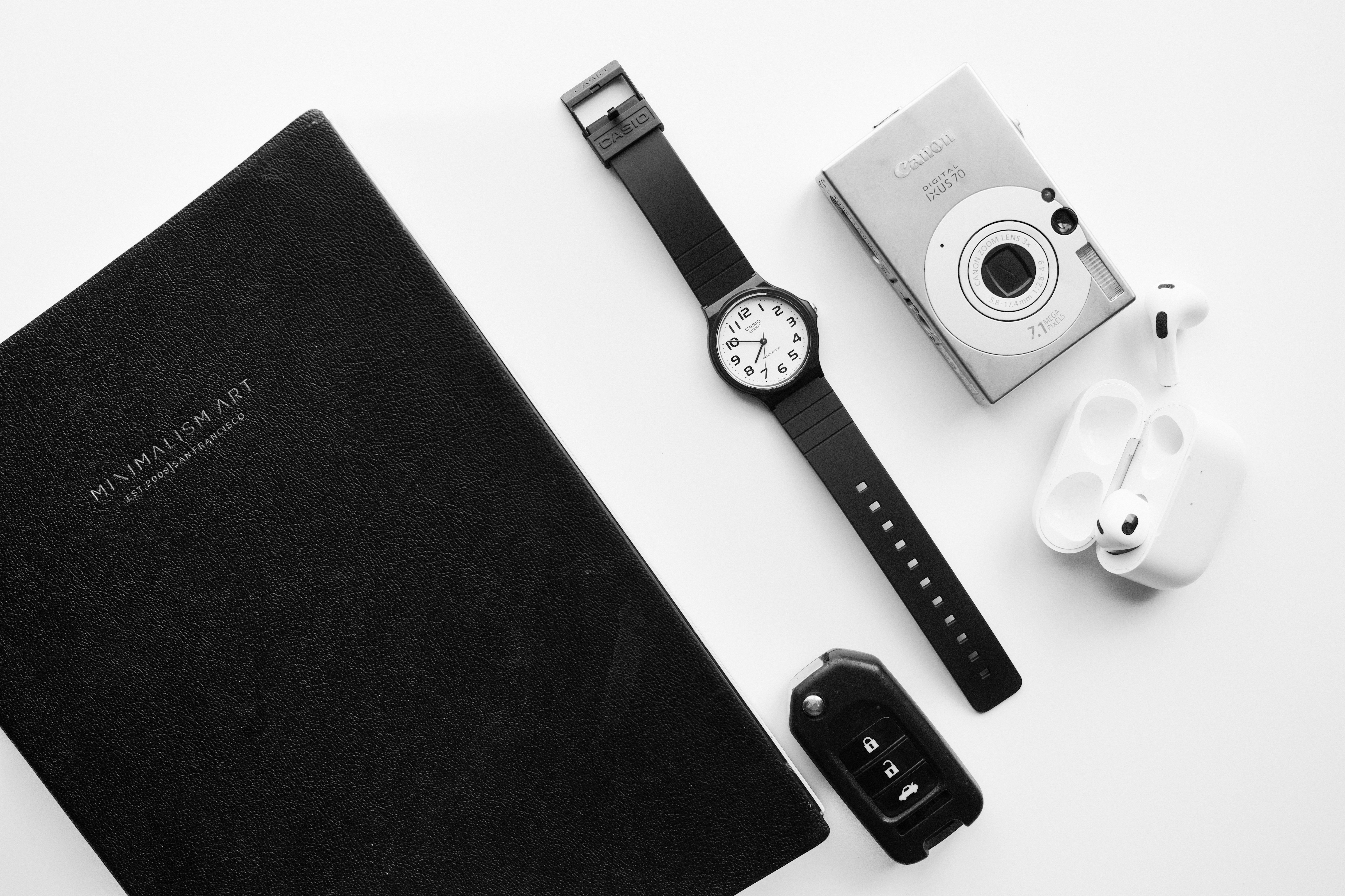 Black notebook, watch, camera, earbuds, and car keys arranged.