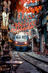 Train approaching narrow street lined with cafes and flags
