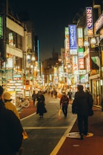 People walking down a brightly lit street at night.