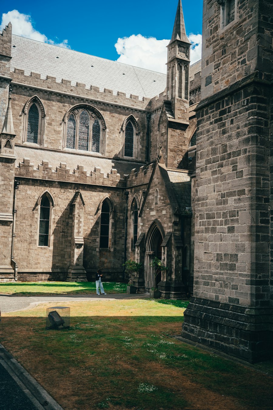 A single visitor crosses a grass courtyard beside a stone Gothic cathedral