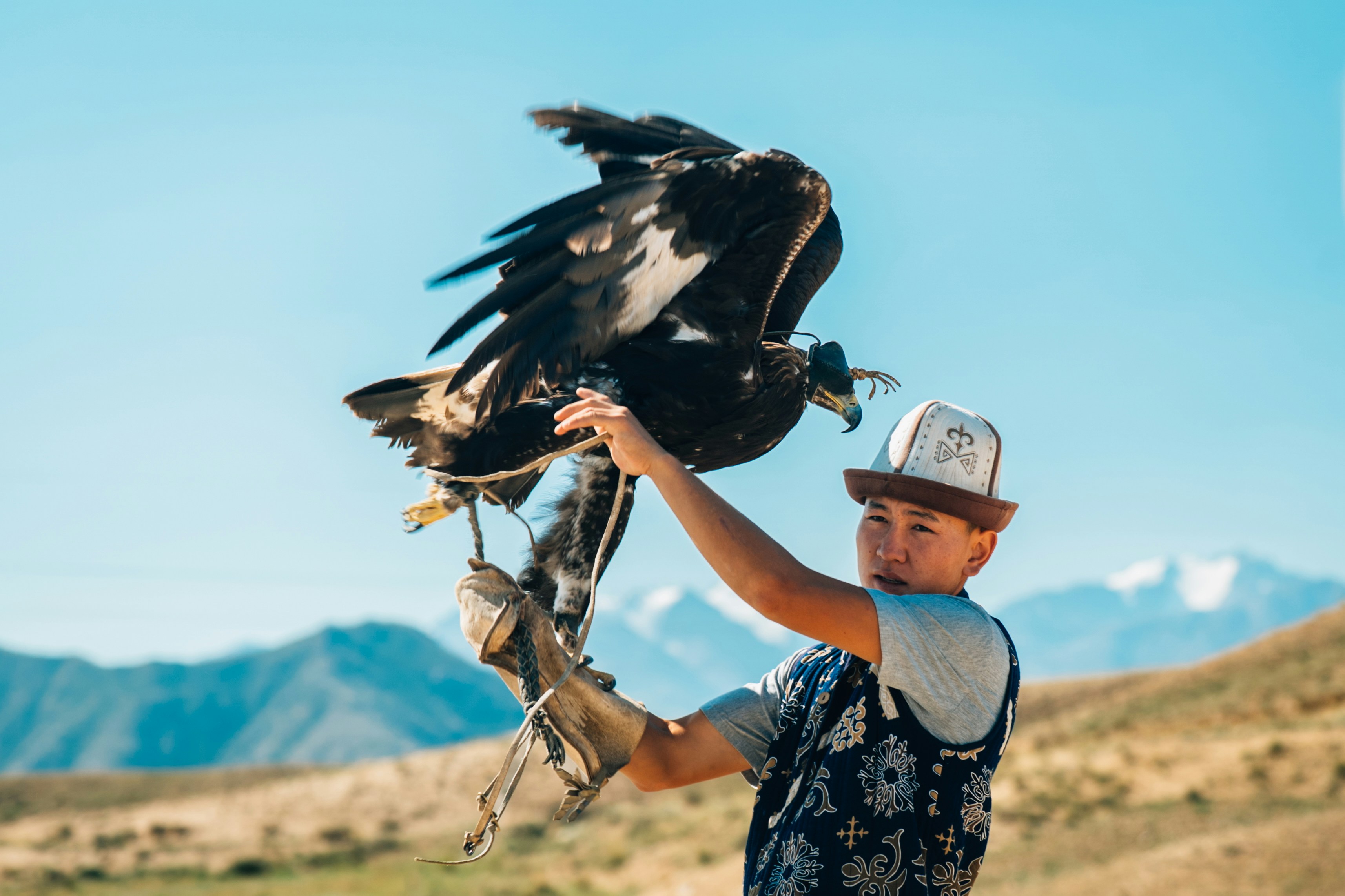 Mann hält einen großen Adler mit Bergen dahinter
