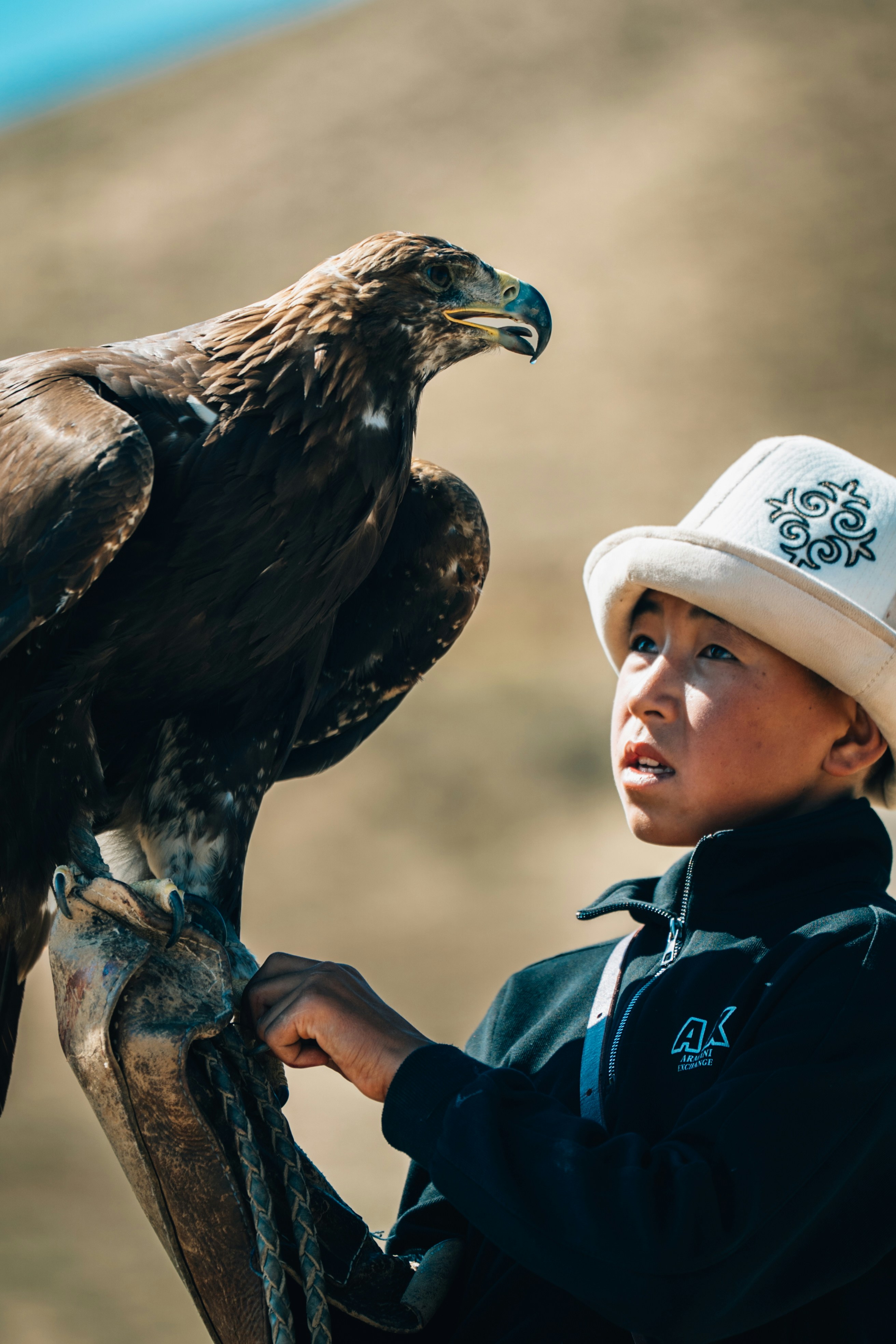 Ein junger Junge hält einen großen Adler mit einem traditionellen Hut.