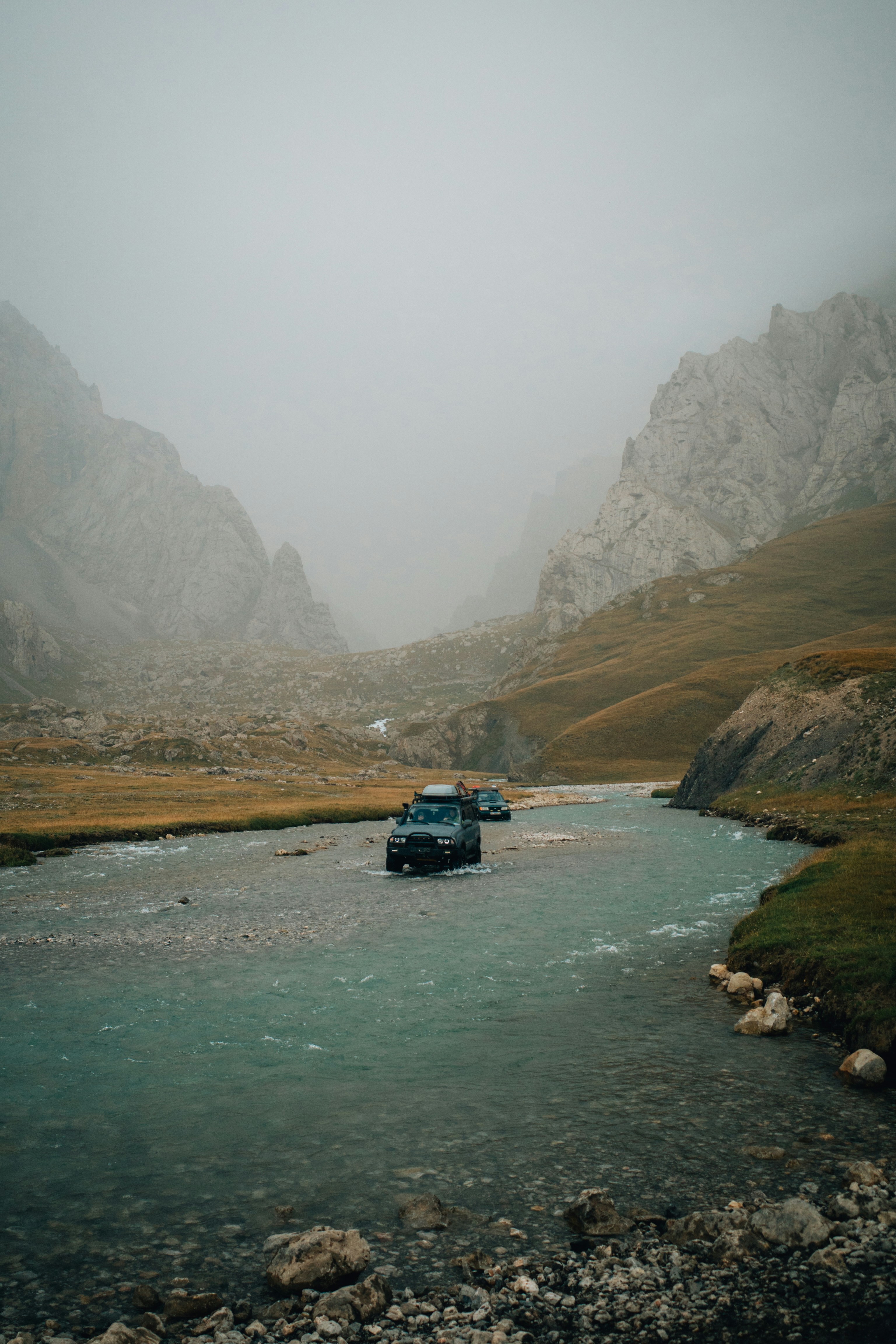 Zwei SUVs fahren durch einen flachen Fluss in einem Bergtal.