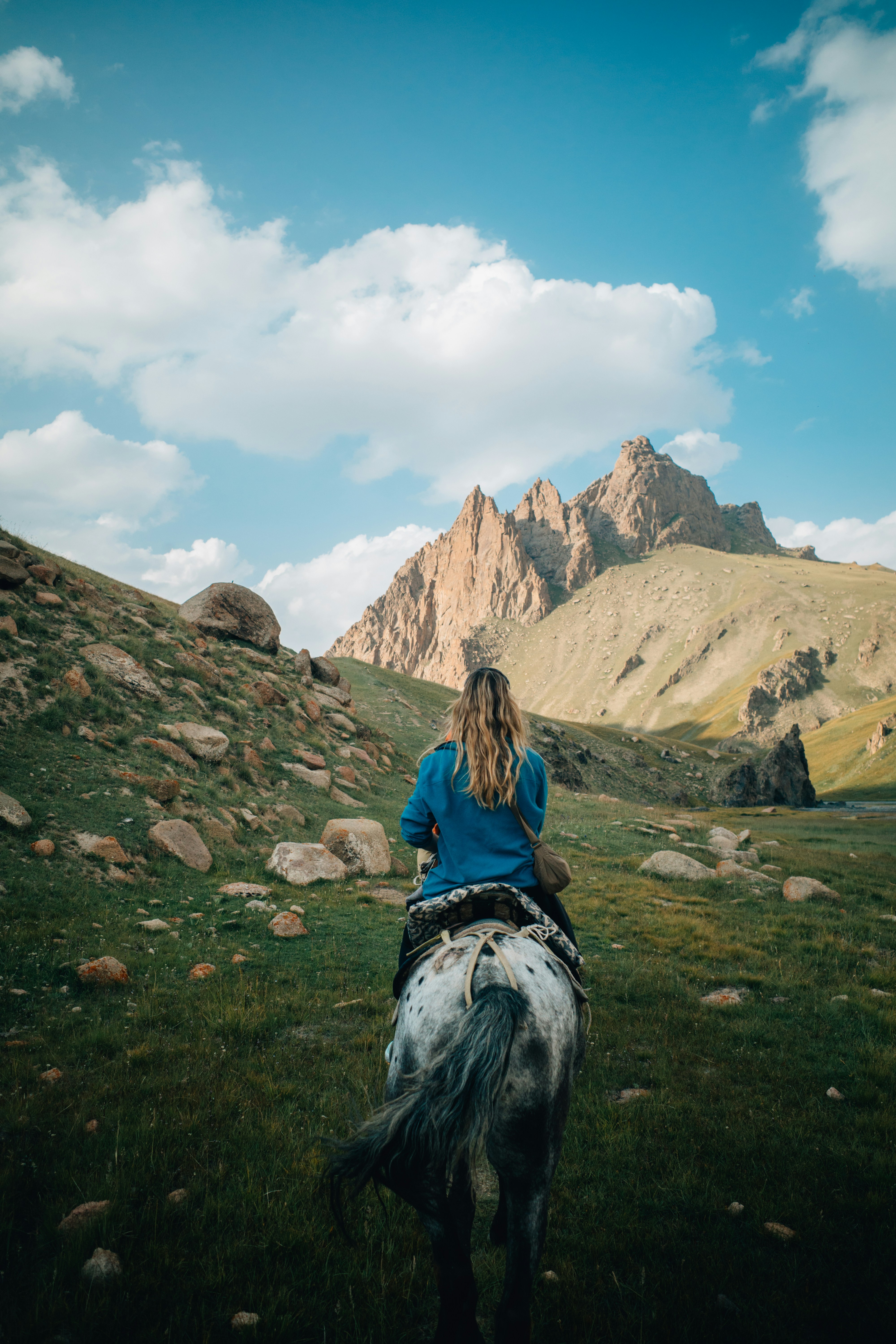 Frau reitet Pferd in Richtung felsige Berge unter Wolken