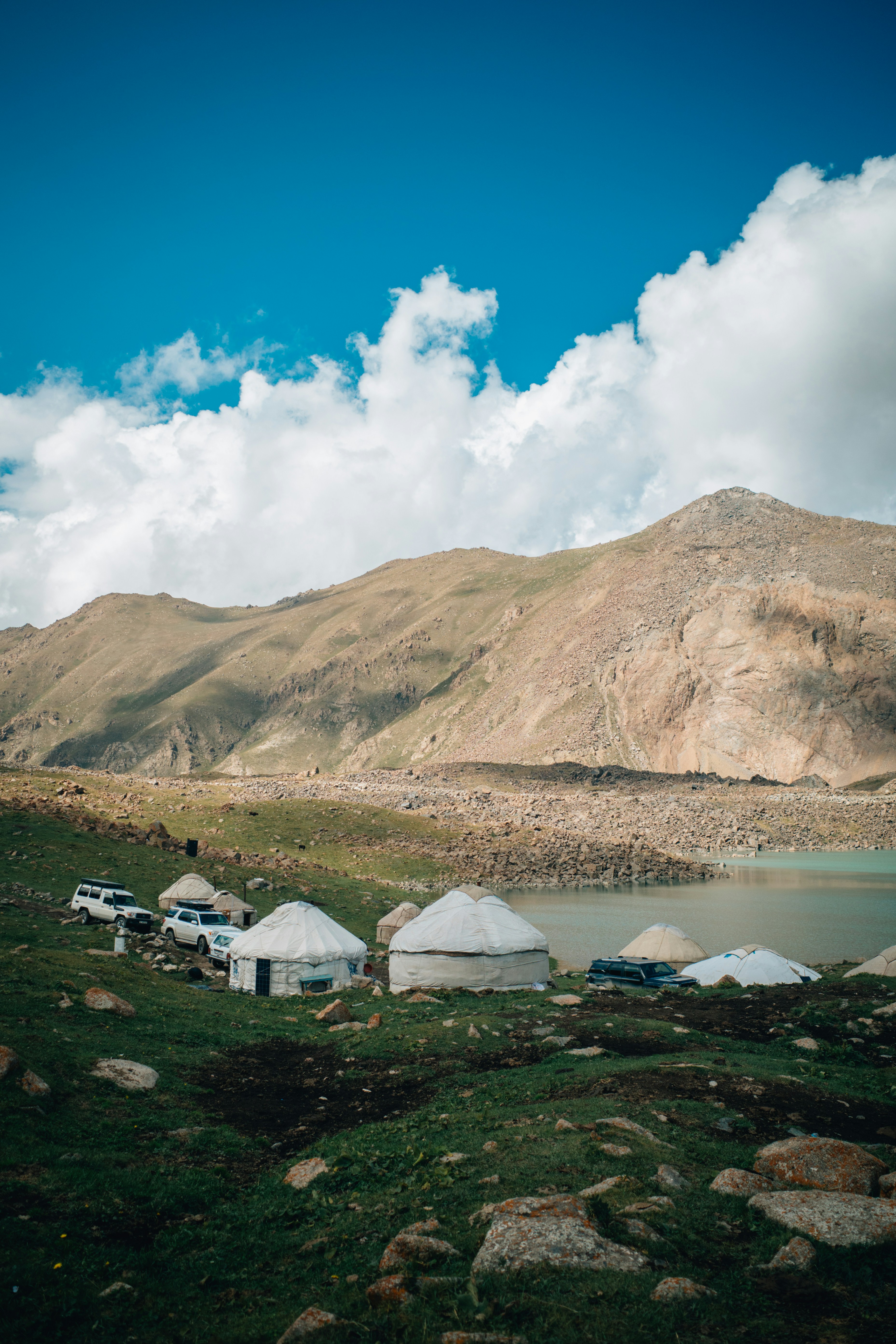 Jurten und Fahrzeuge an einem See mit Bergen