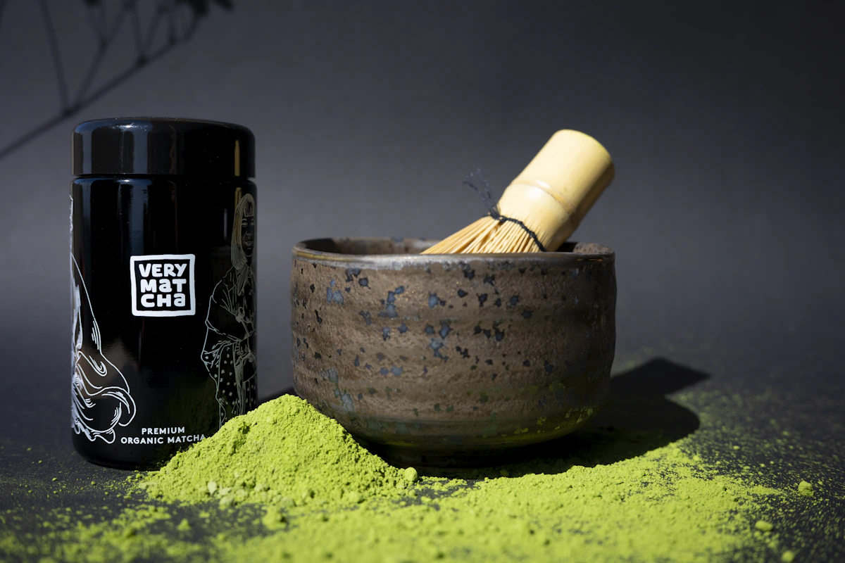 Matcha-Pulver mit Bambusbesen und Behälter auf dunkler Holzfläche bereit zur Zubereitung