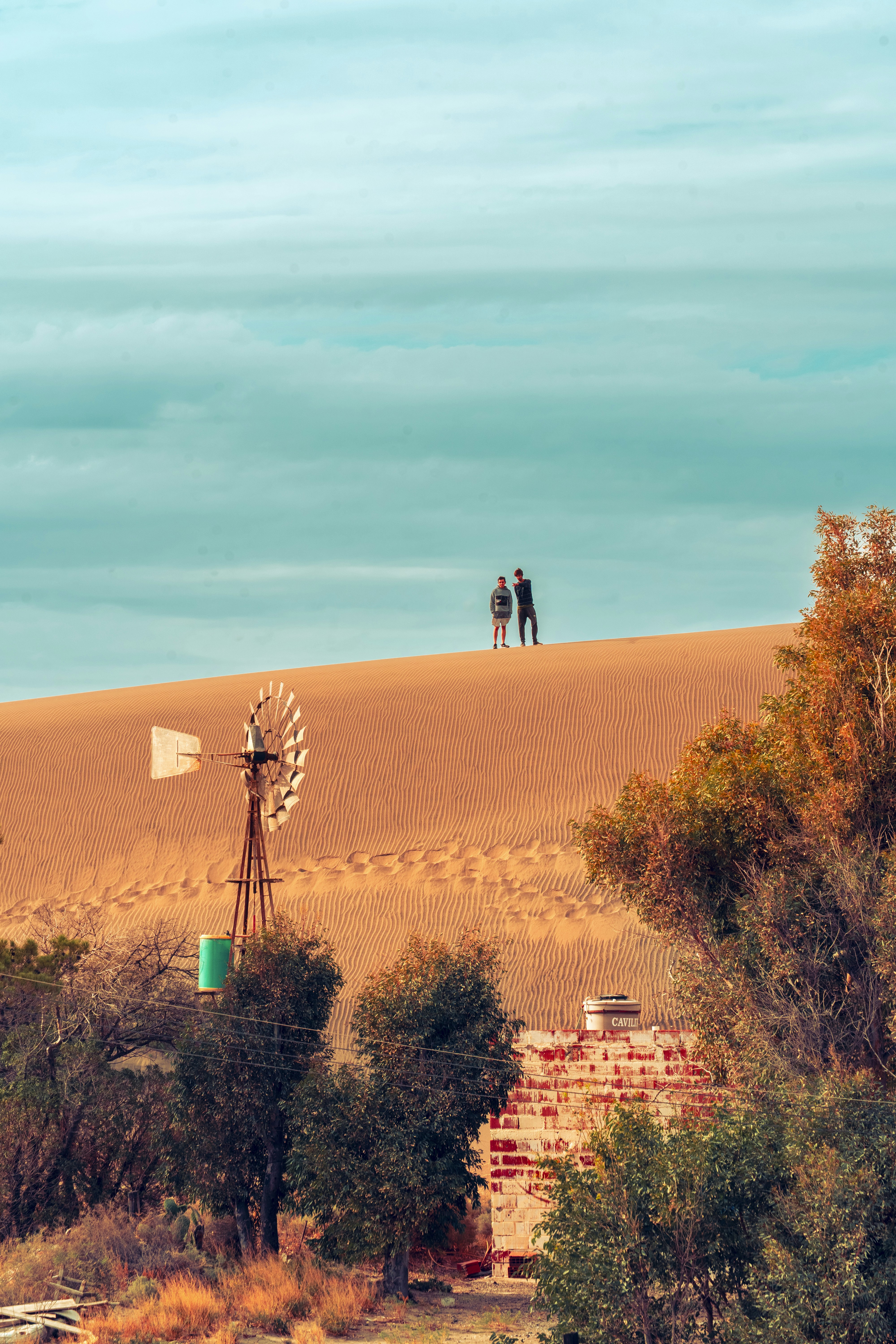 Two people on a sand dune with a windmill.