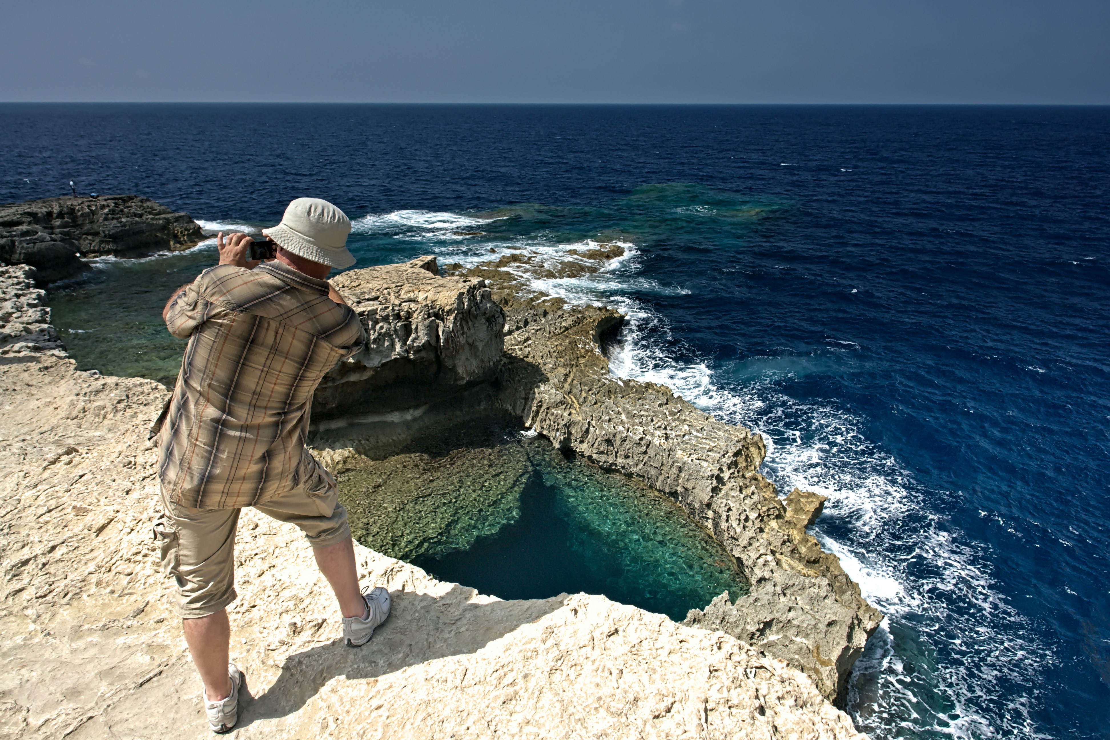 Man photographing rocky coastline with blue ocean