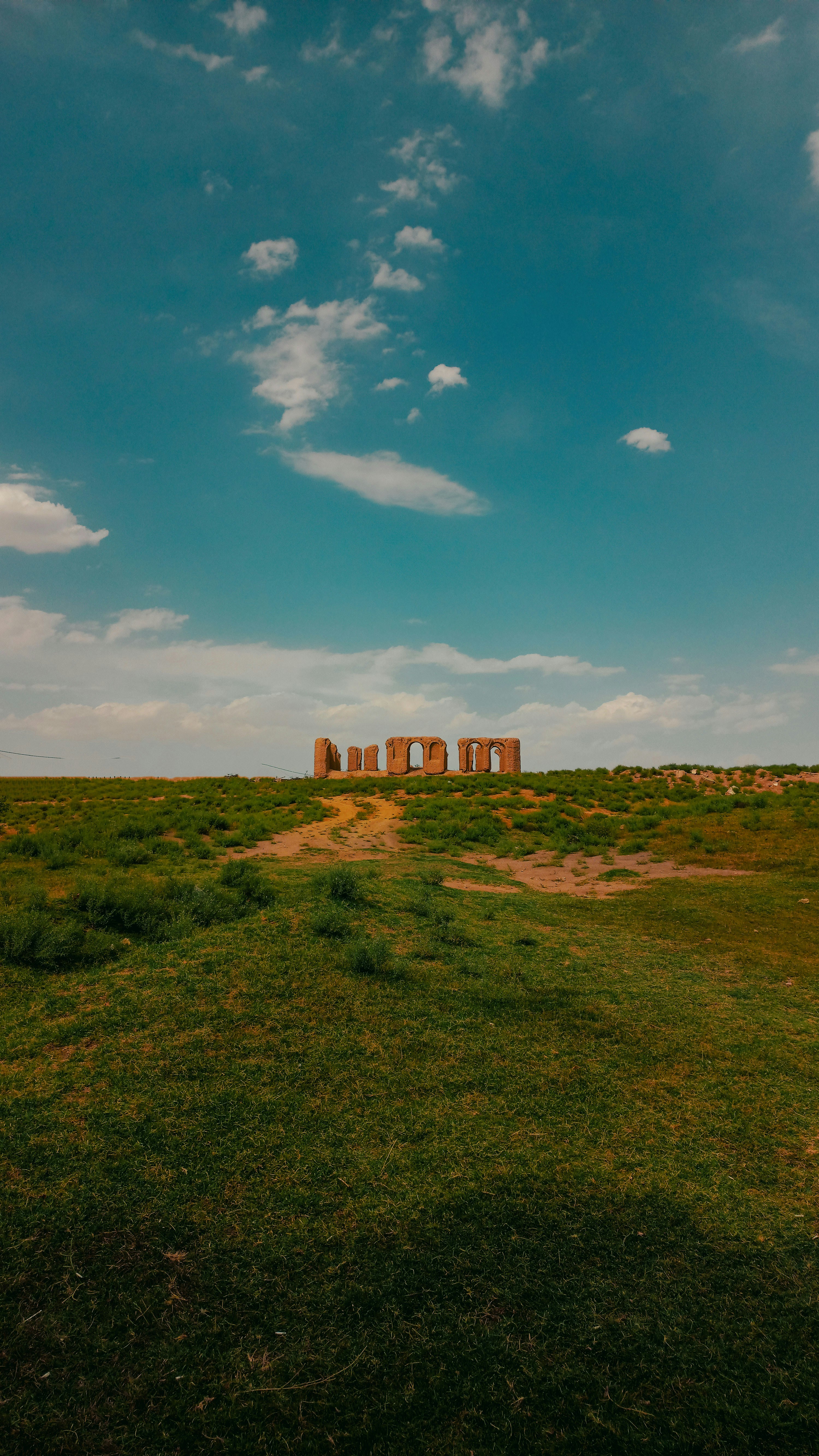 Ancient ruins stand on a grassy hill under a blue sky.