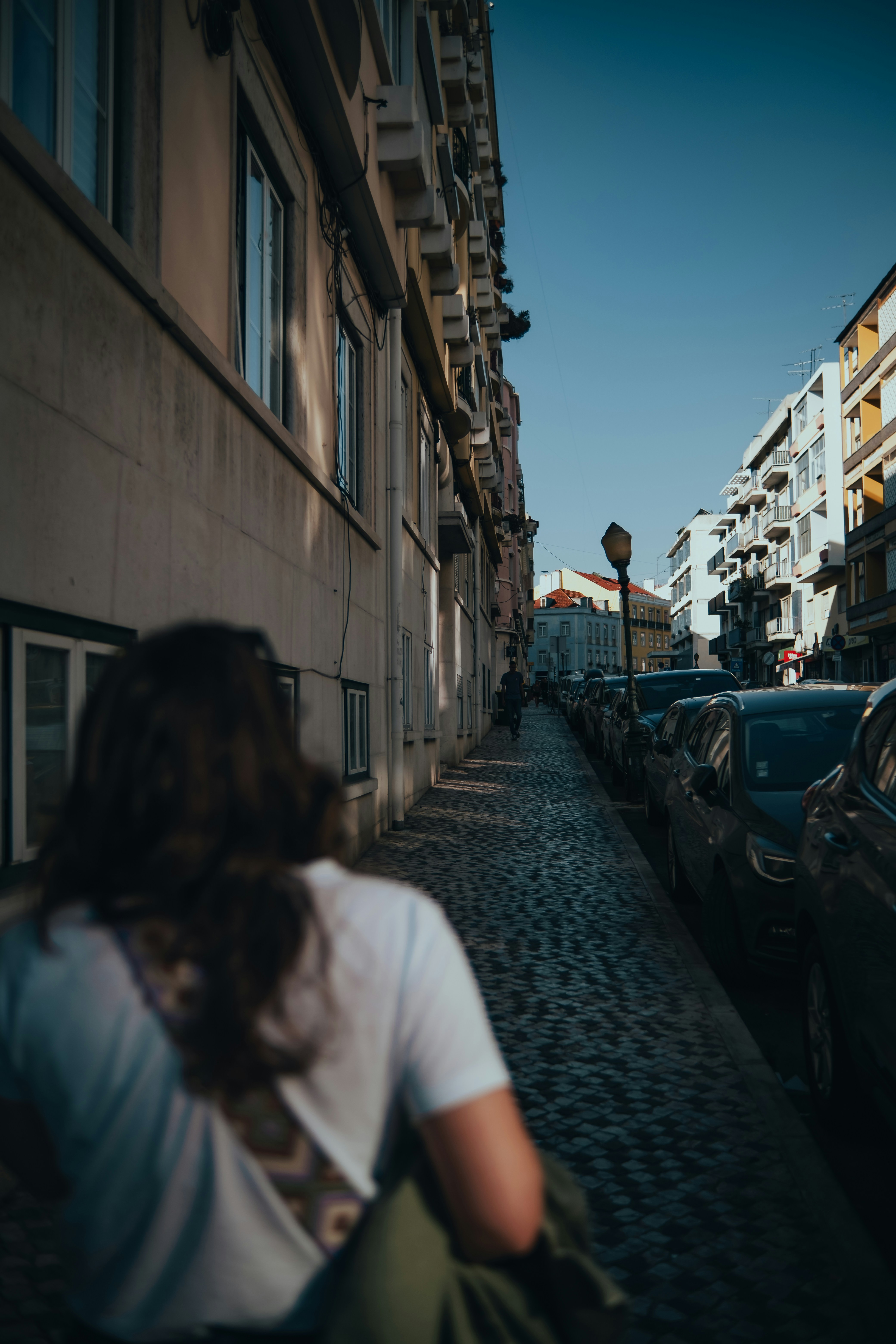 Eine Person geht eine Kopfsteinpflasterstraße entlang, die von Autos gesäumt ist.