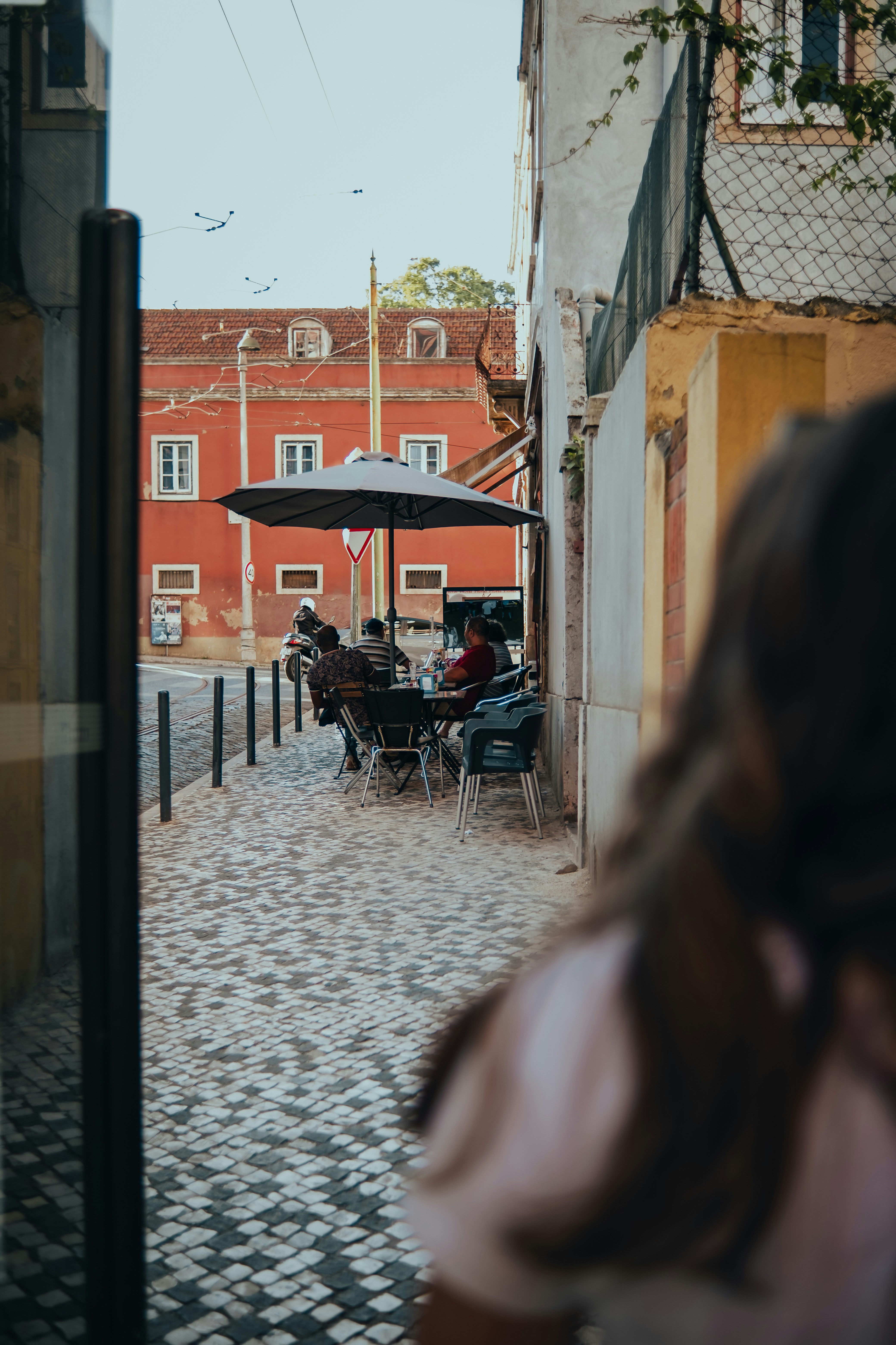 Menschen sitzen an Tischen vor einem Café in einer Kopfsteinpflasterstraße.