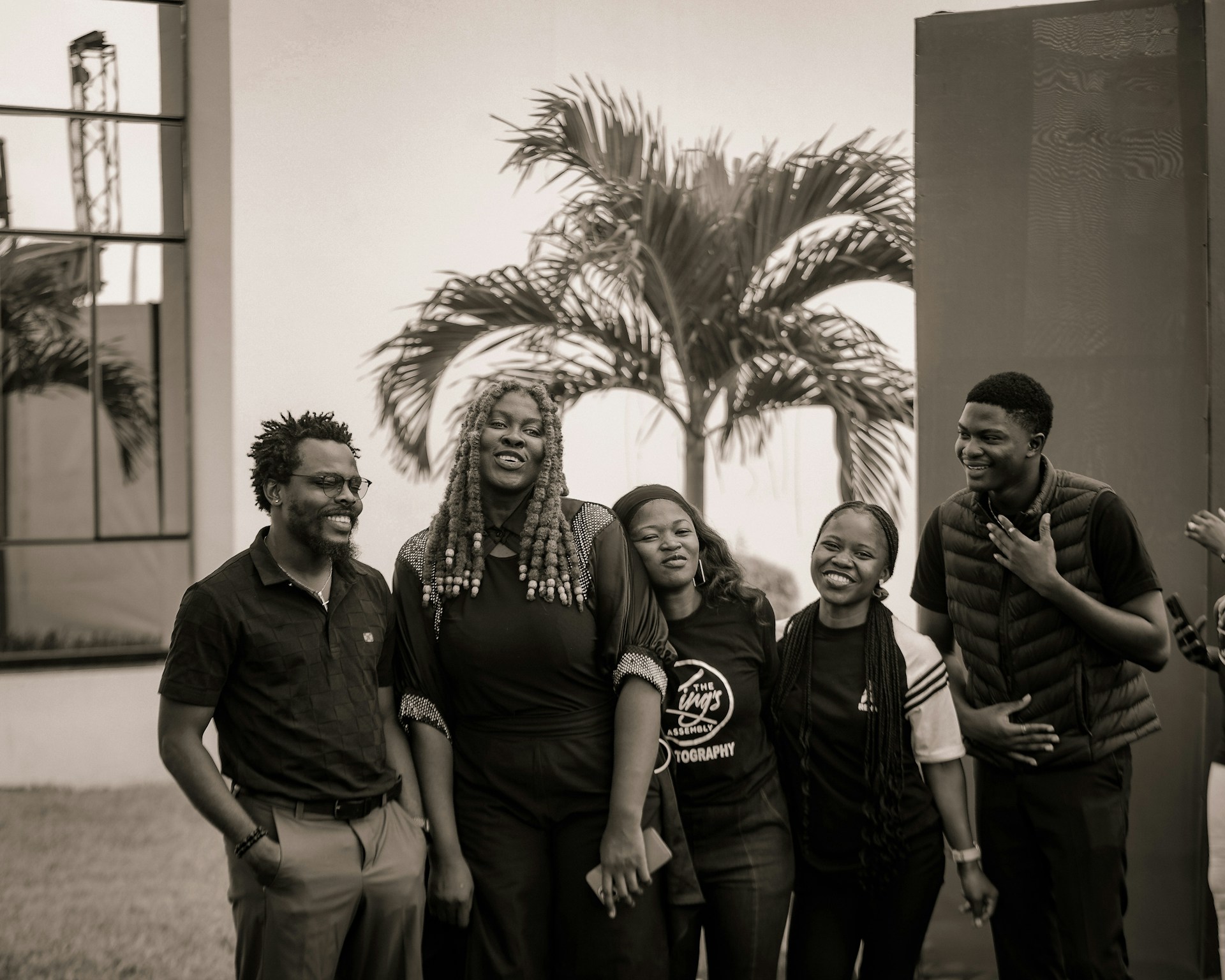 Group of five people smiling outdoors with palm tree