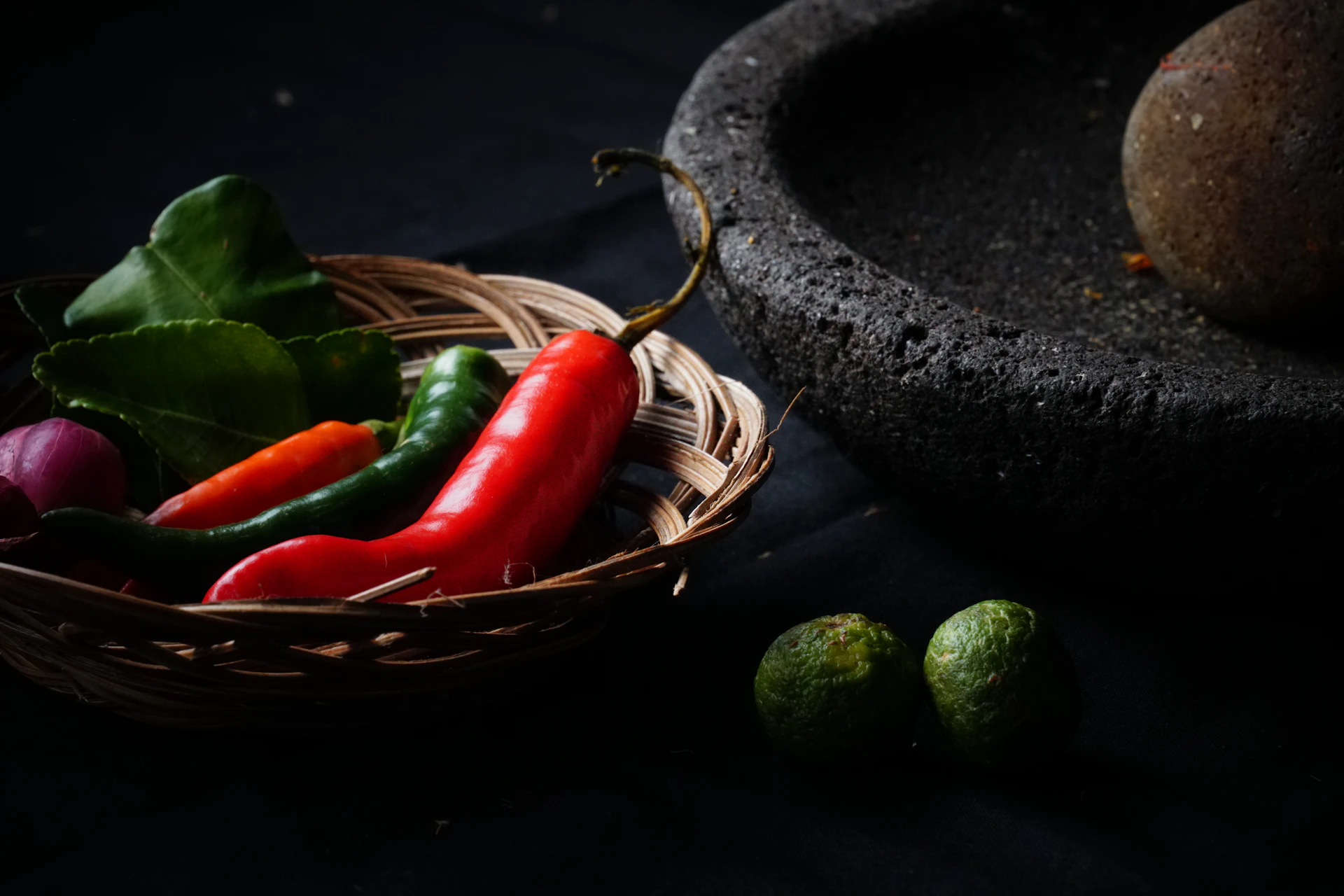 Chili peppers, lime, and herbs in a basket with mortar