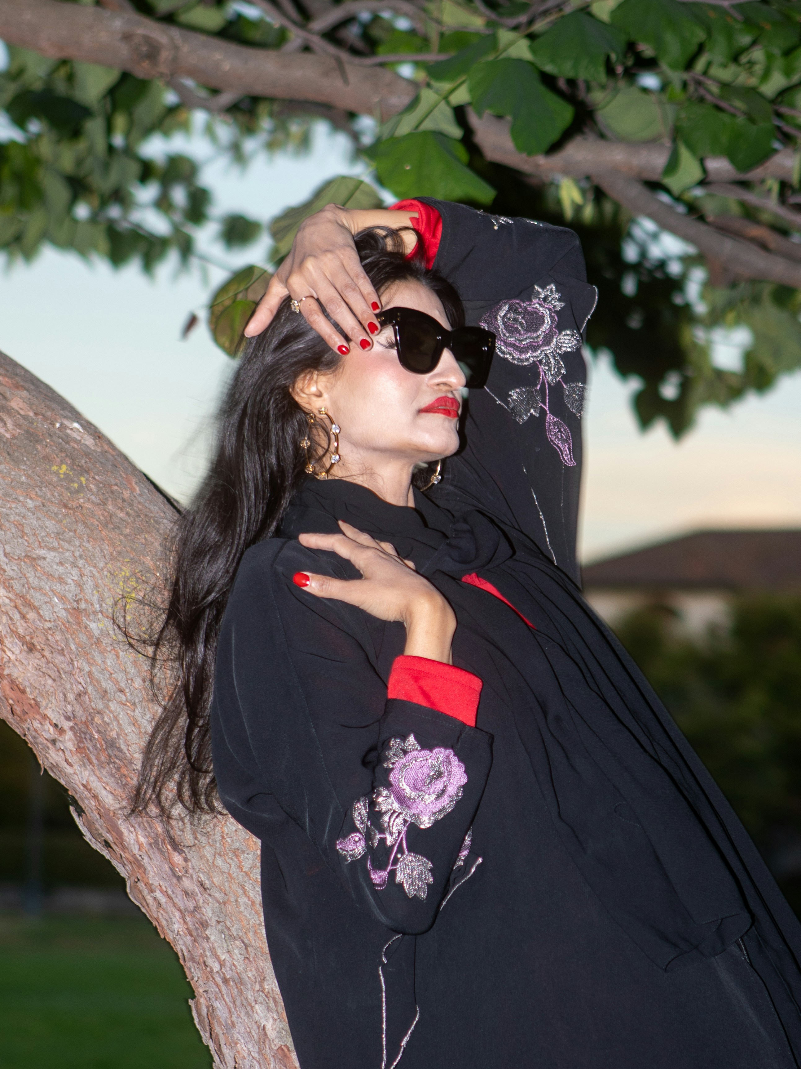 Mujer con elegante traje negro posa cerca del árbol