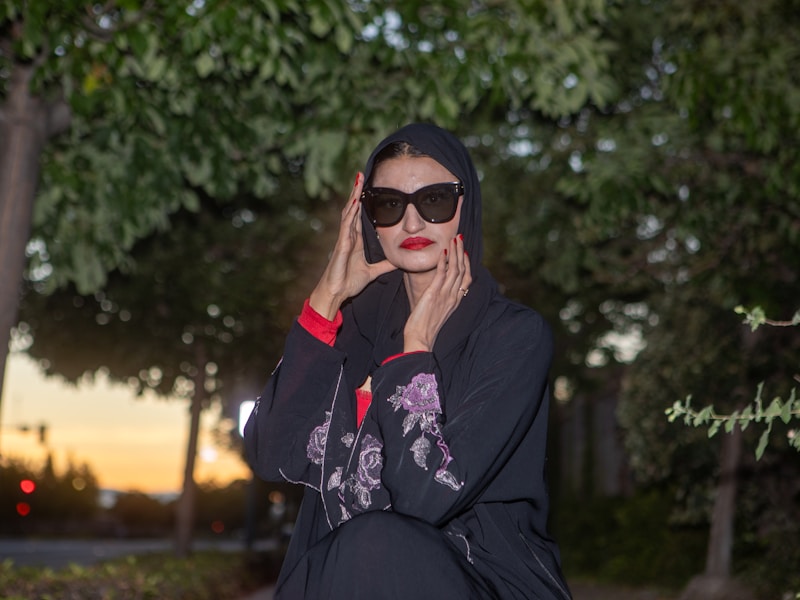 Woman in black abaya with sunglasses poses outdoors.