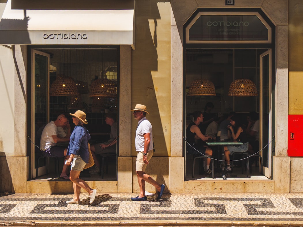 People walking past a corner cafe in a sunny European city street, the kind of place a long-term resident treats as their second living room