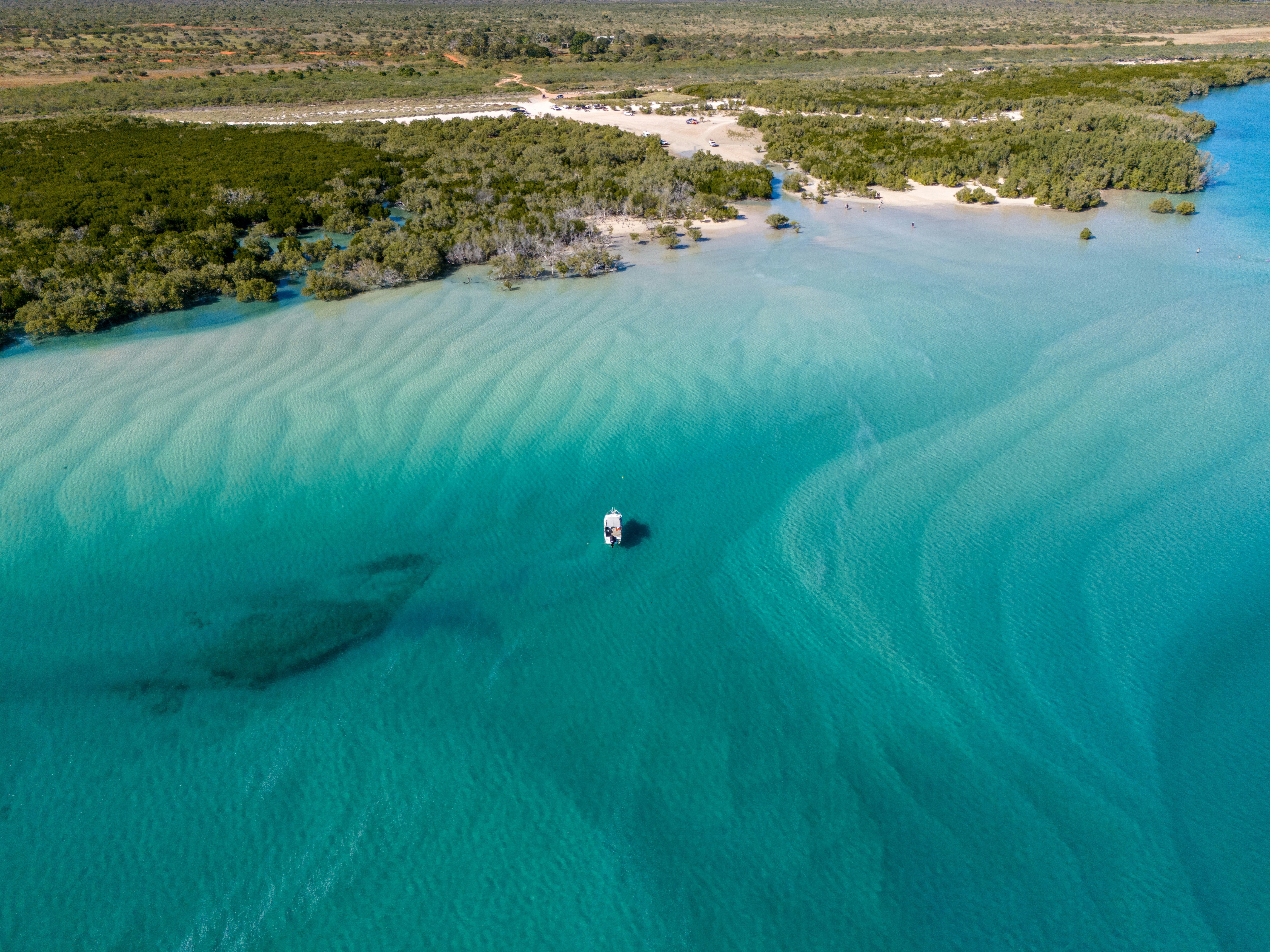 Una piccola barca galleggia su acque turchesi con banchi di sabbia