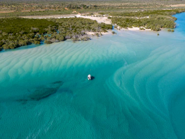 Small boat floats on turquoise water with sandbars.