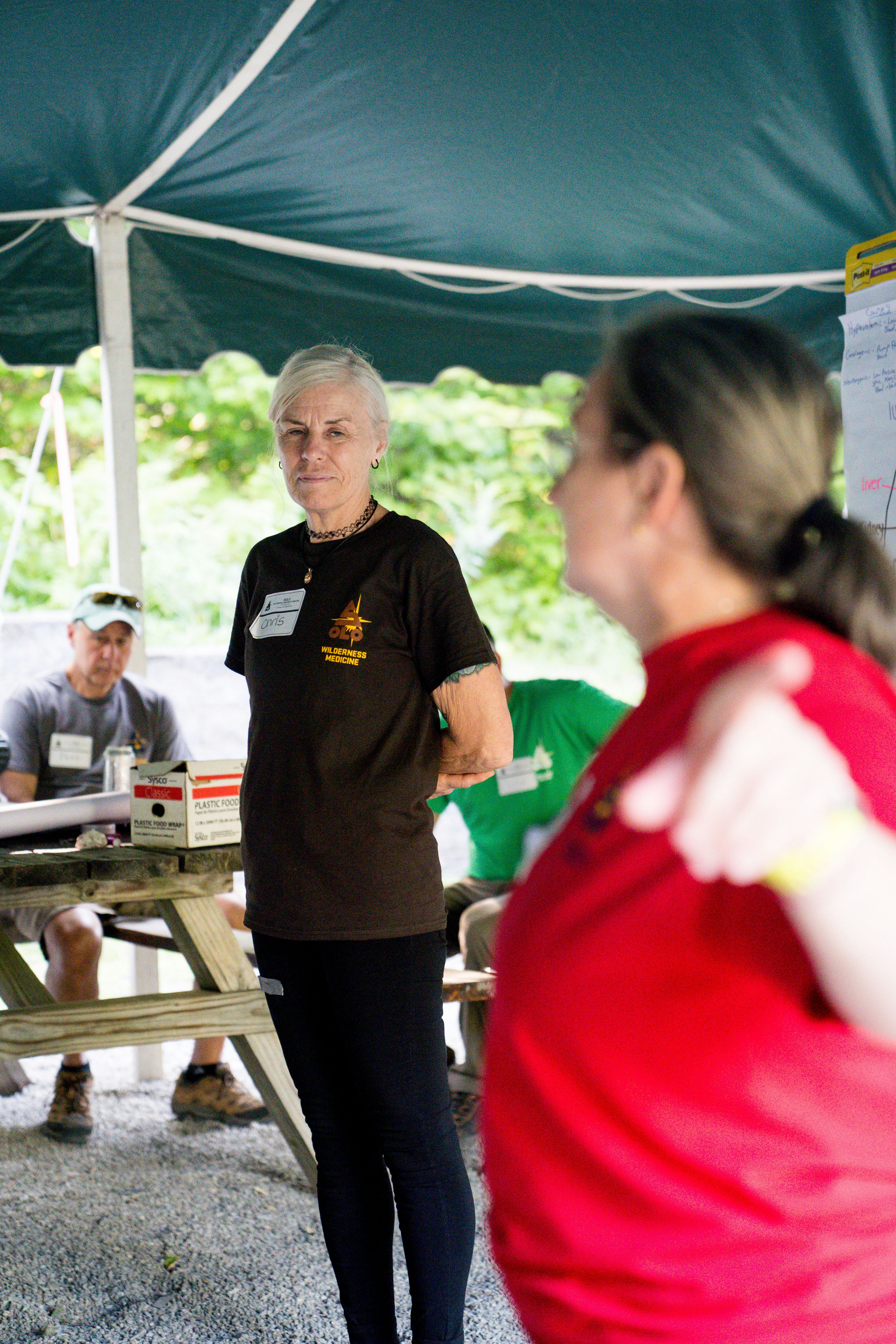 Woman in brown shirt addresses group under tent