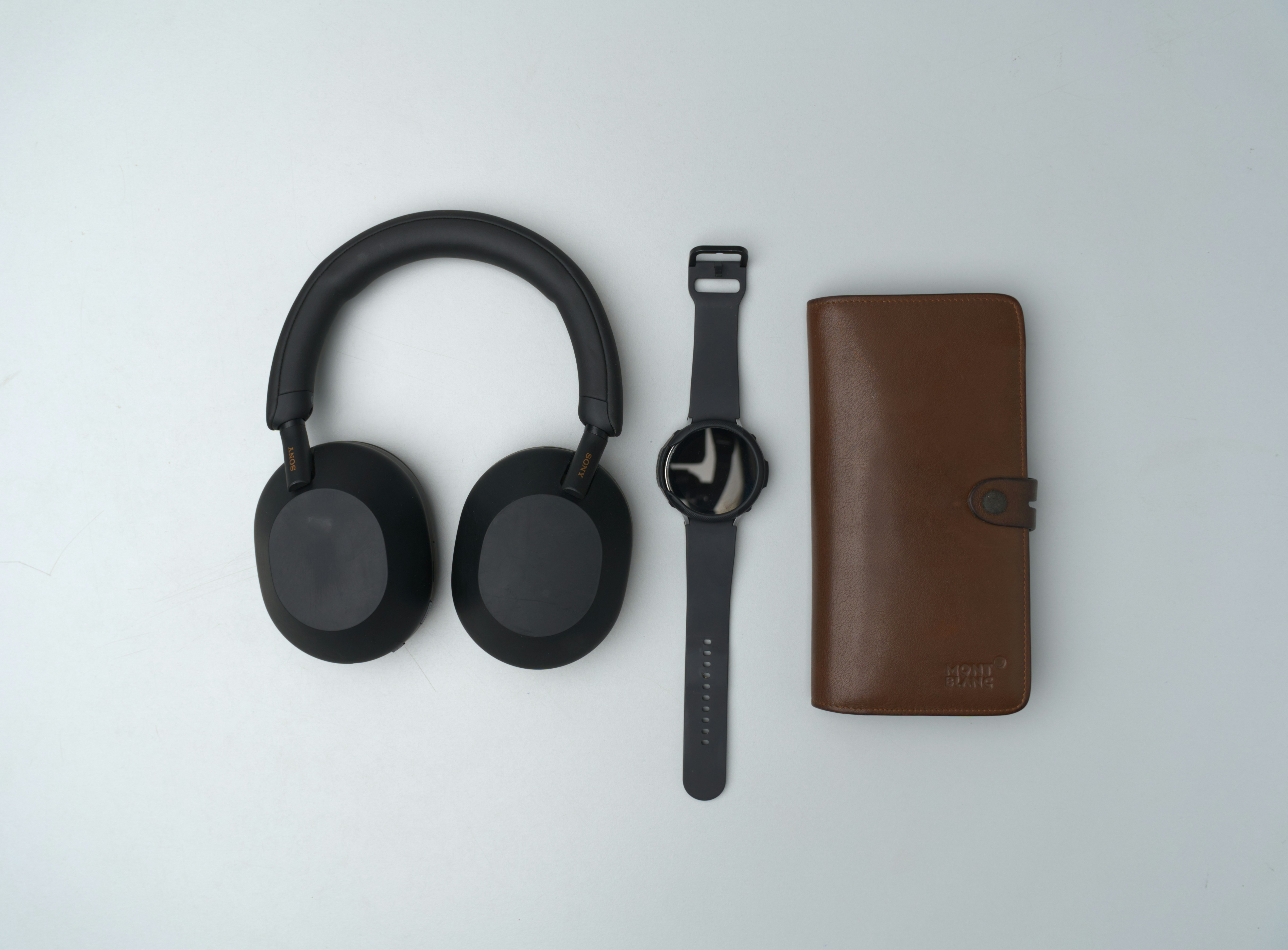 Black headphones, wristwatch, and brown wallet arranged neatly., 