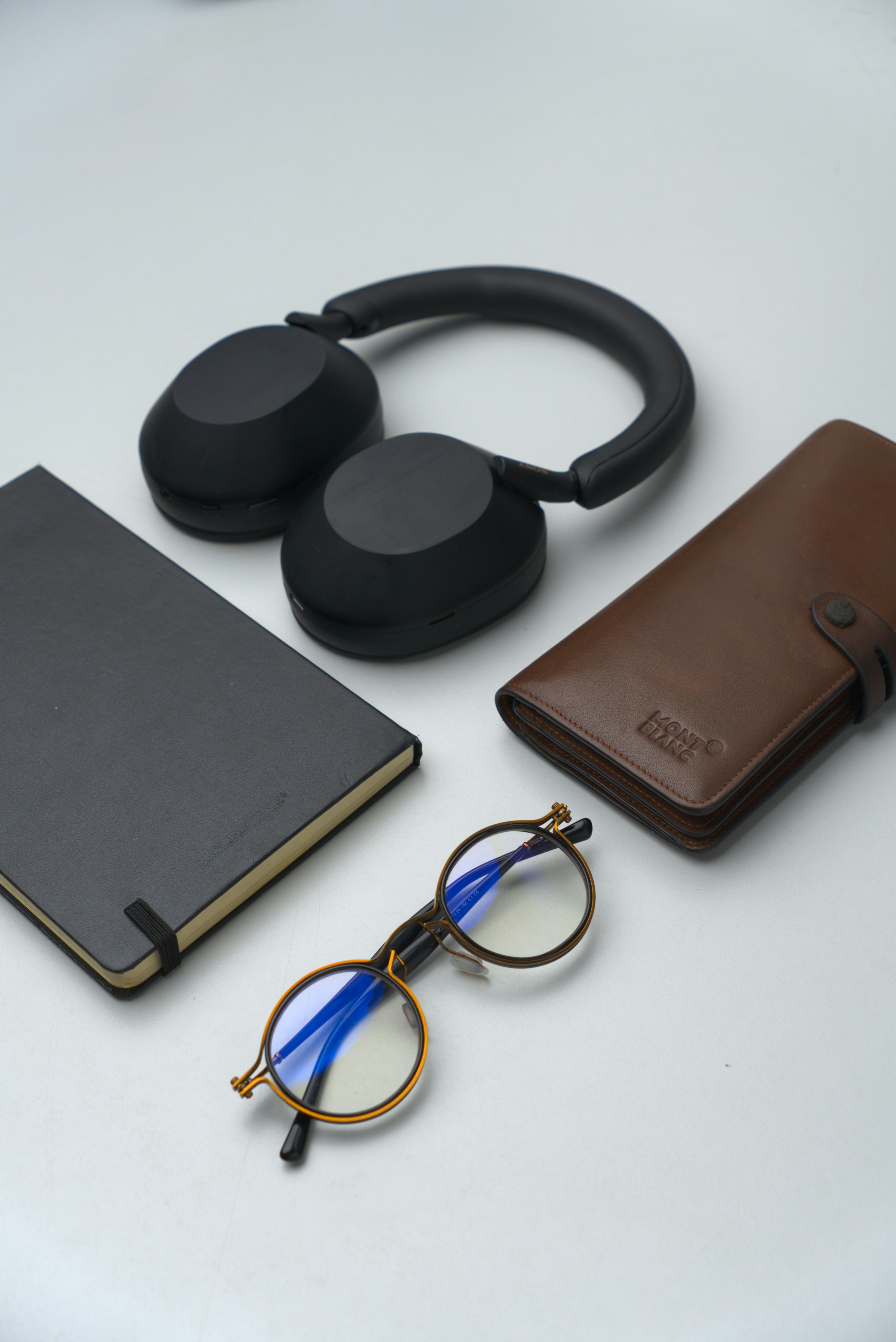 A minimalist flat lay of my everyday carry items— wallet, notebook, spectacles, and headphones—carefully arranged on a white surface. A visual reflection of simplicity and order in daily life.